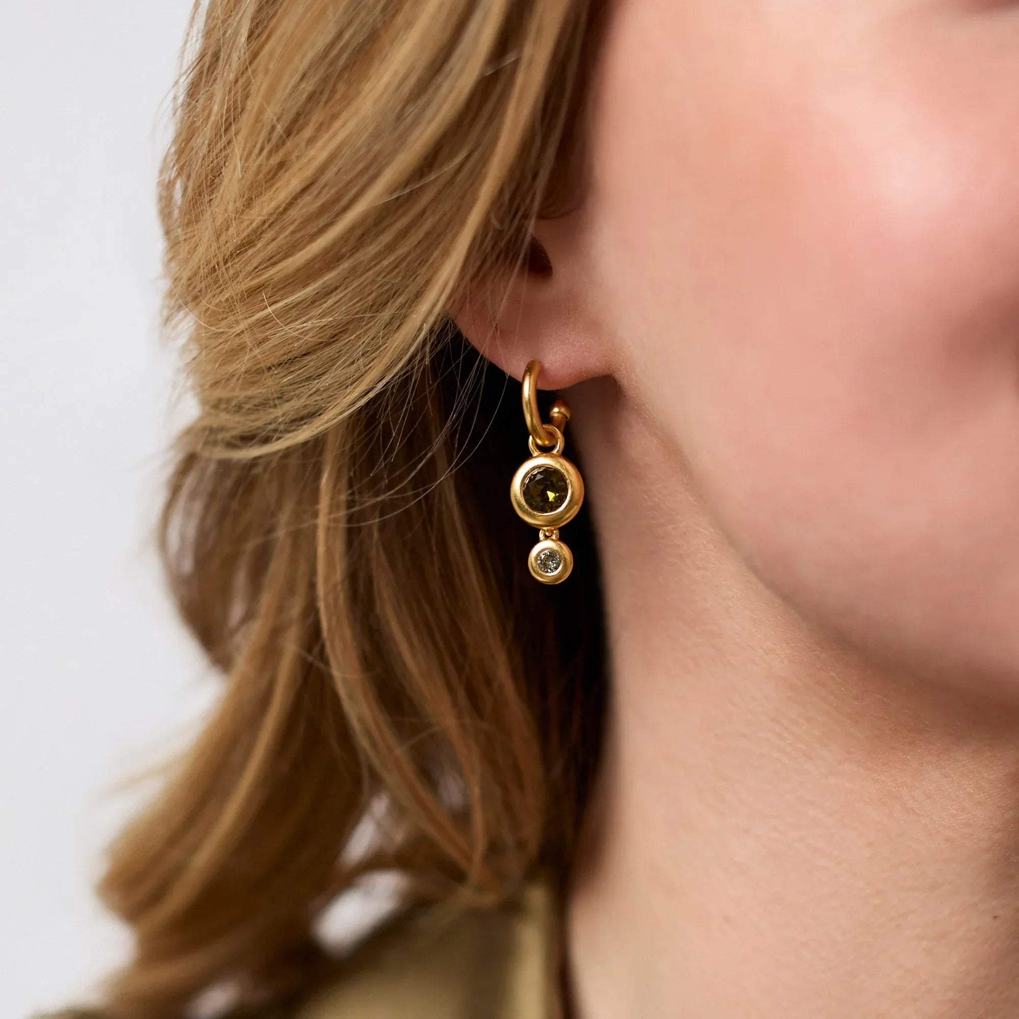 Close-up of a person wearing gold earrings with a neutral background