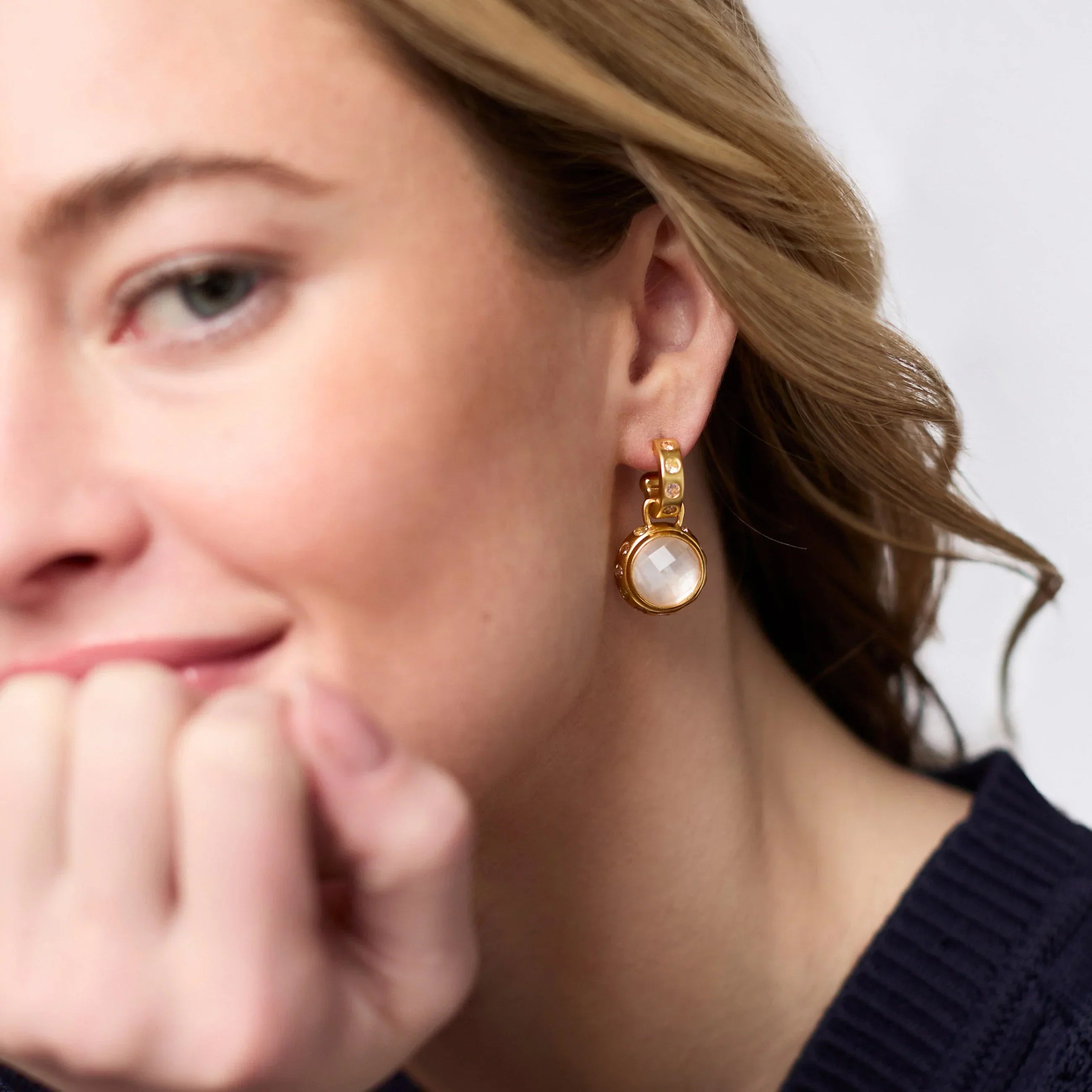 Close-up of a person wearing a gold earring with a white stone.