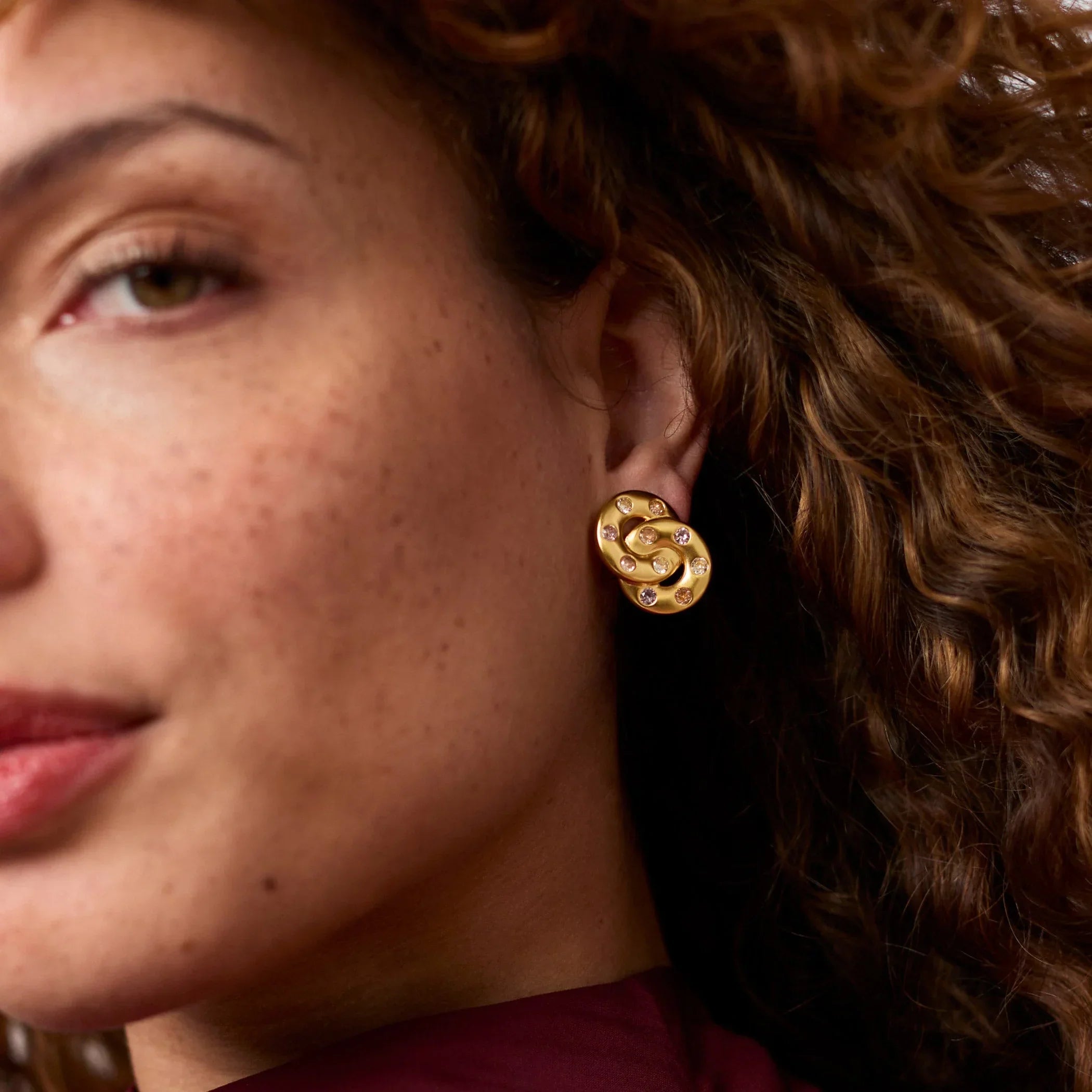 Close-up of a woman wearing gold earrings with a maroon top.