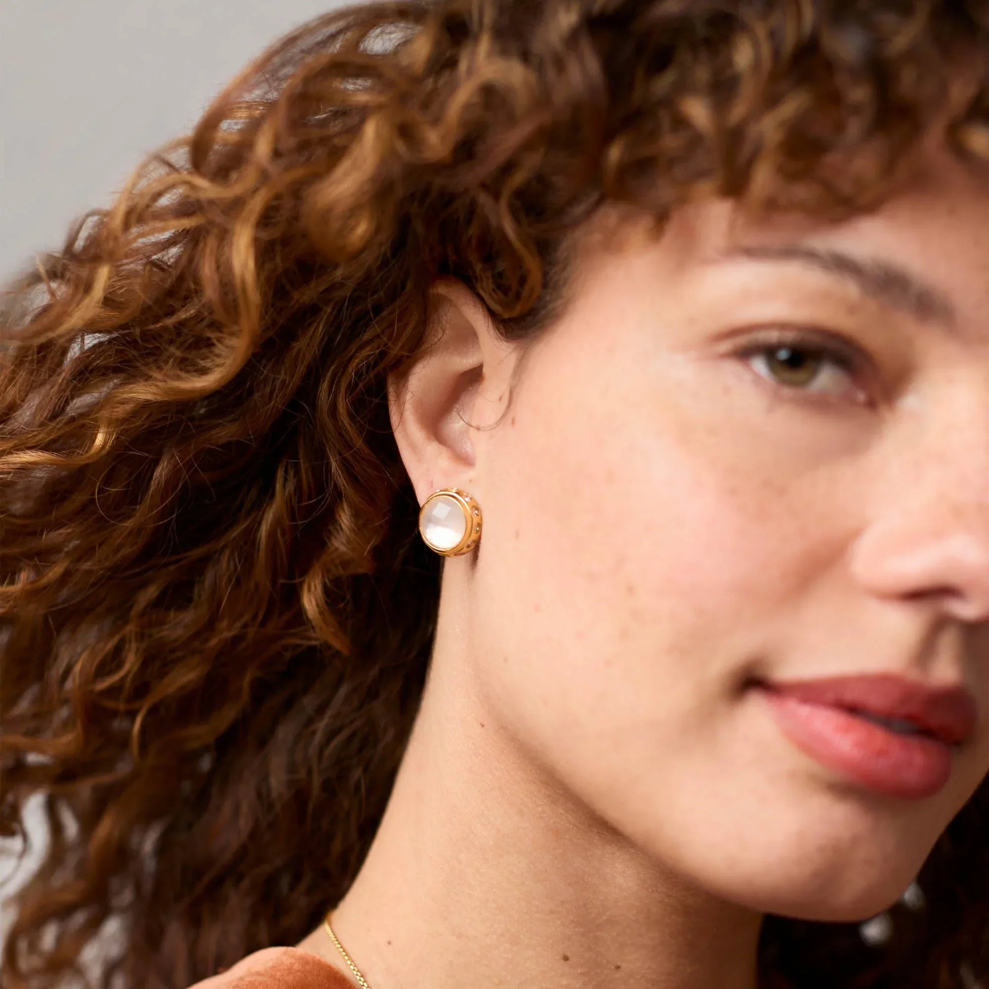 Close-up of a person wearing a gold earring with a clear gemstone.