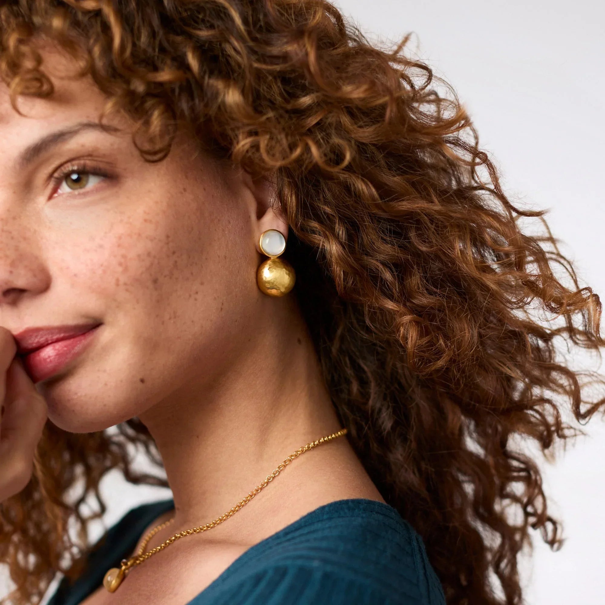 Close-up of a woman wearing gold earrings and necklace against a neutral background