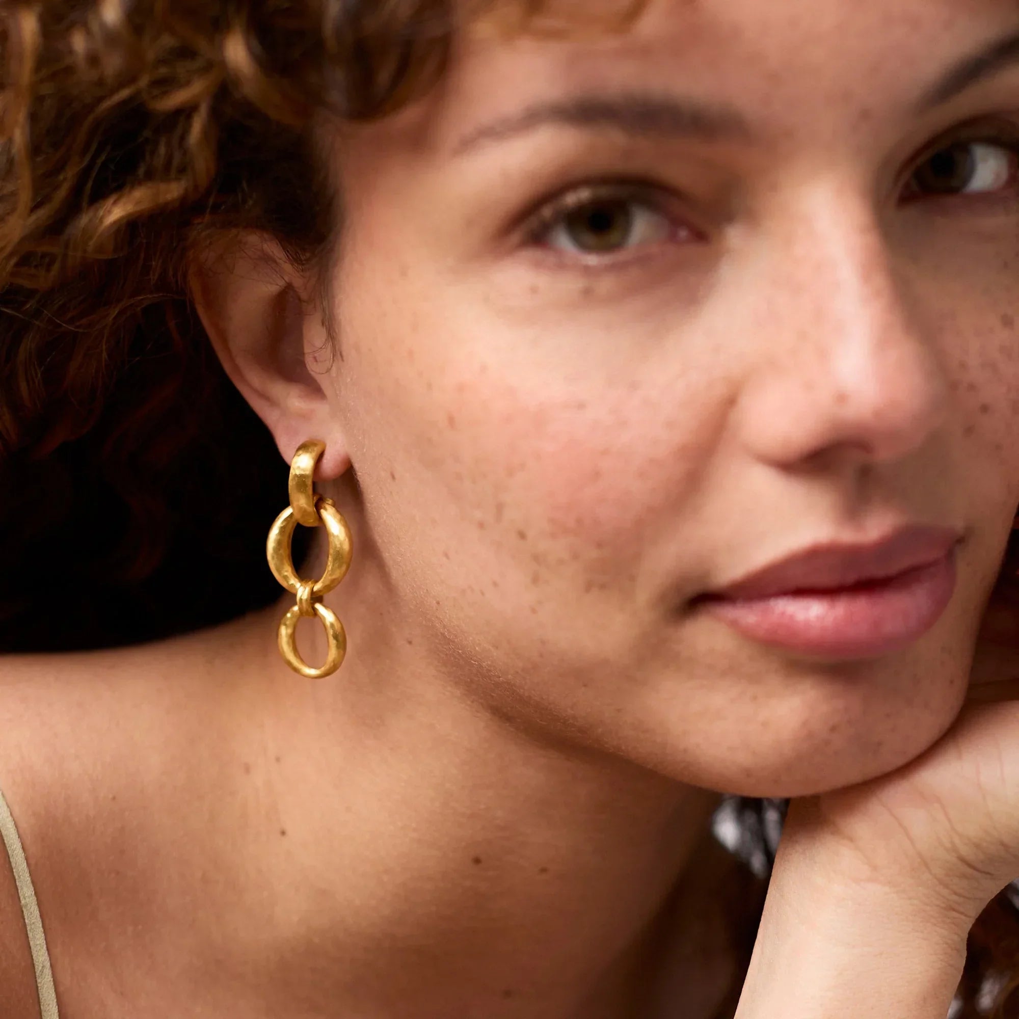 Close-up of a woman wearing gold hoop earrings with a blurred background