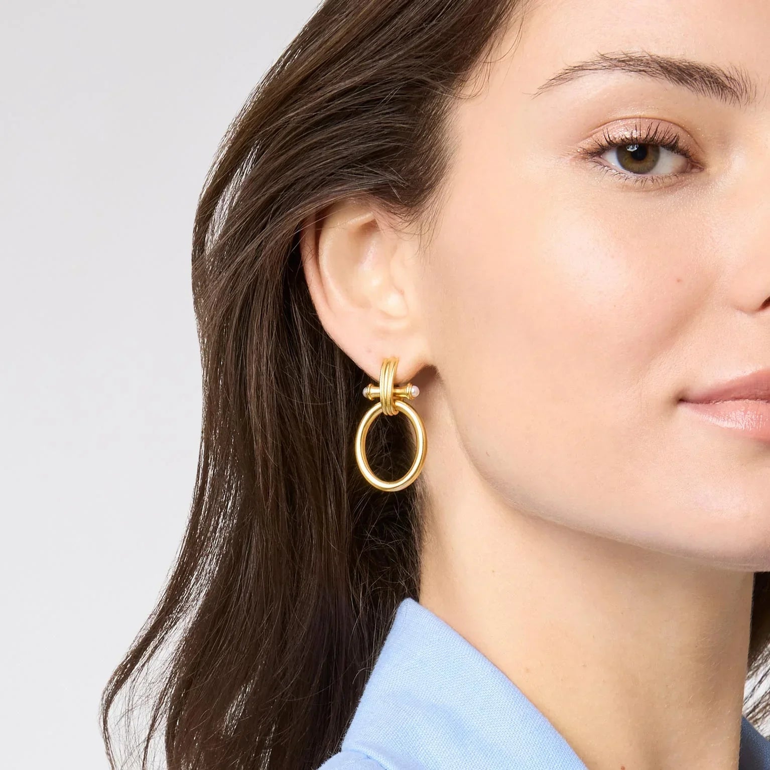 Close-up of a woman wearing gold hoop earrings with a light gray background