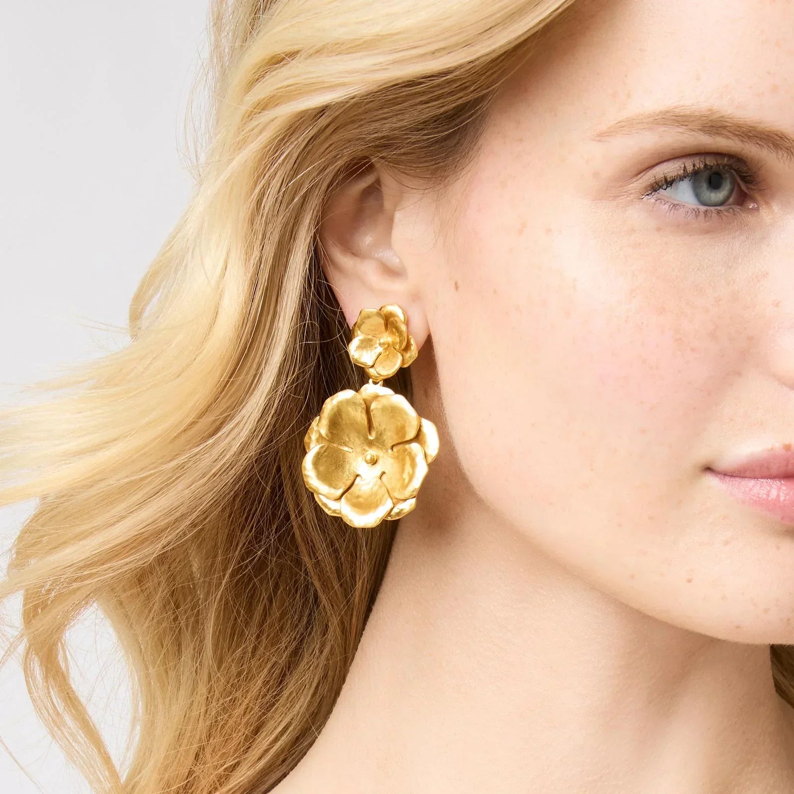 Close-up of a woman wearing gold floral earrings with a plain background