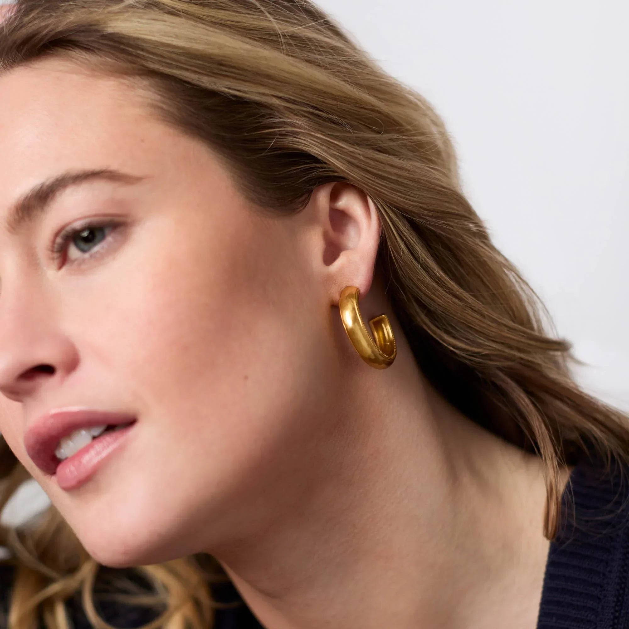 Close-up of a woman wearing gold hoop earrings with a neutral background