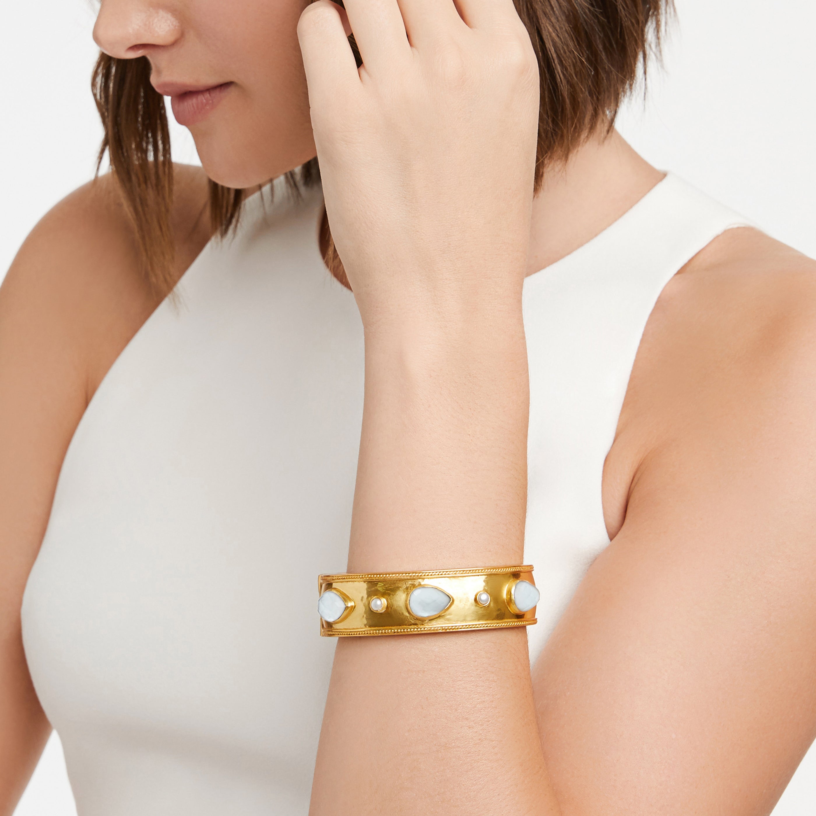 Woman wearing a gold bracelet with white stones on a plain background
