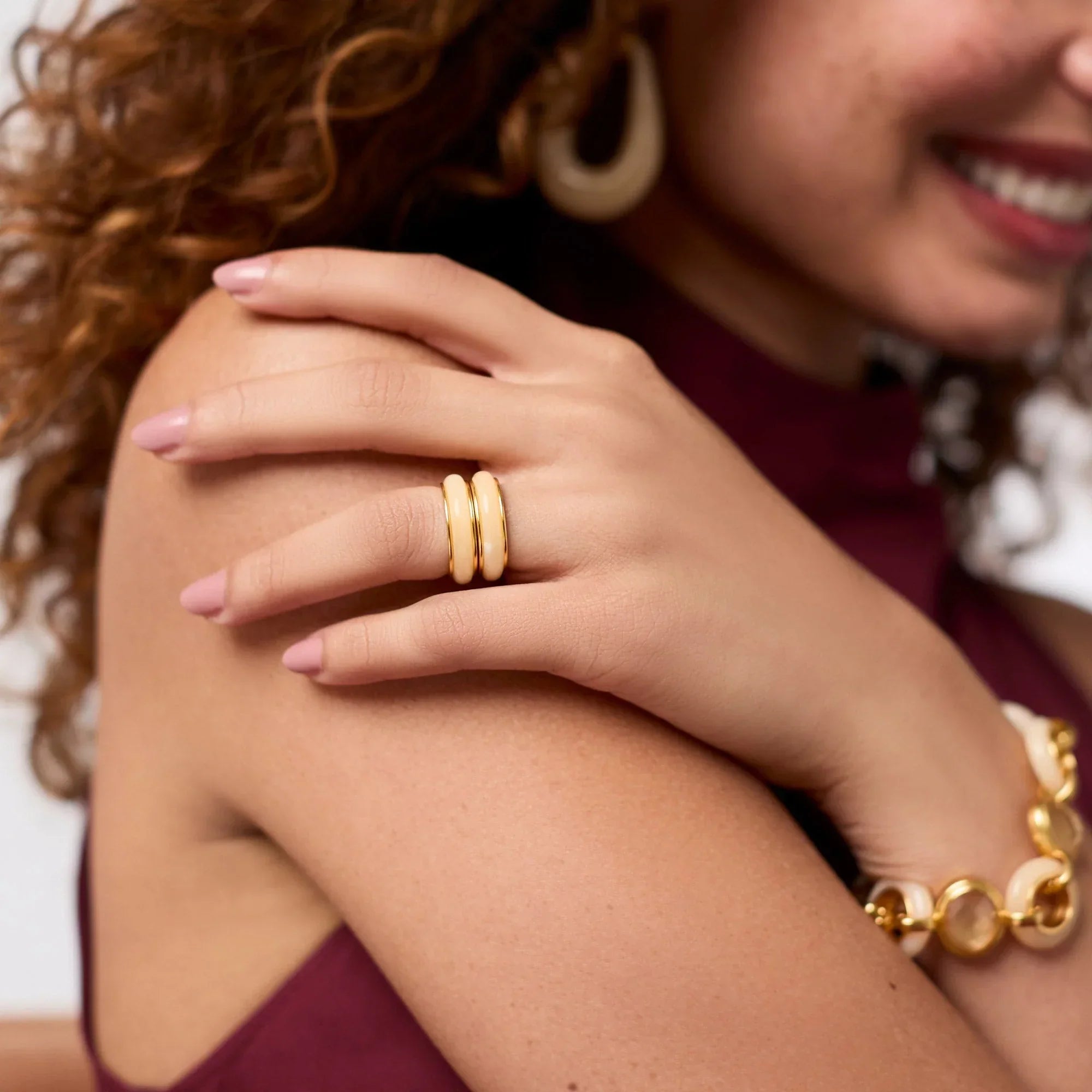 Close-up of a woman's arm with gold rings and bracelet, wearing a burgundy top.