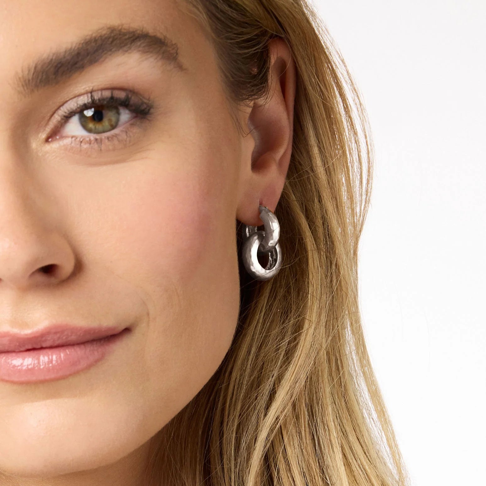Close-up of a woman wearing silver hoop earrings on a white background