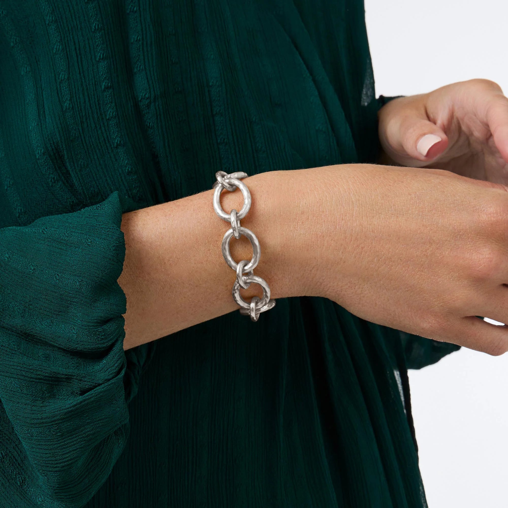 Silver chain bracelet on a person wearing a green dress against a white background