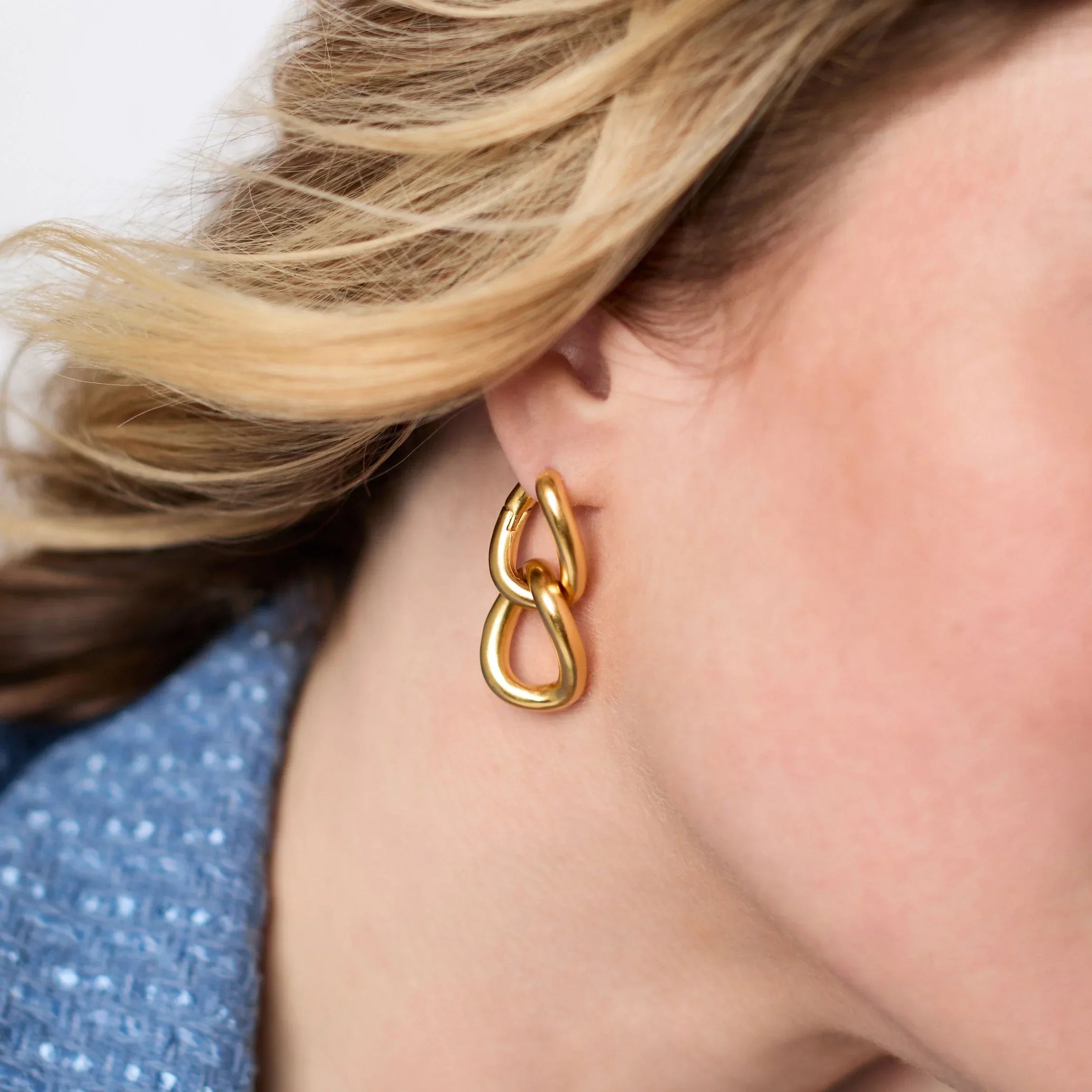 Gold chain earring worn by a person with blonde hair.
