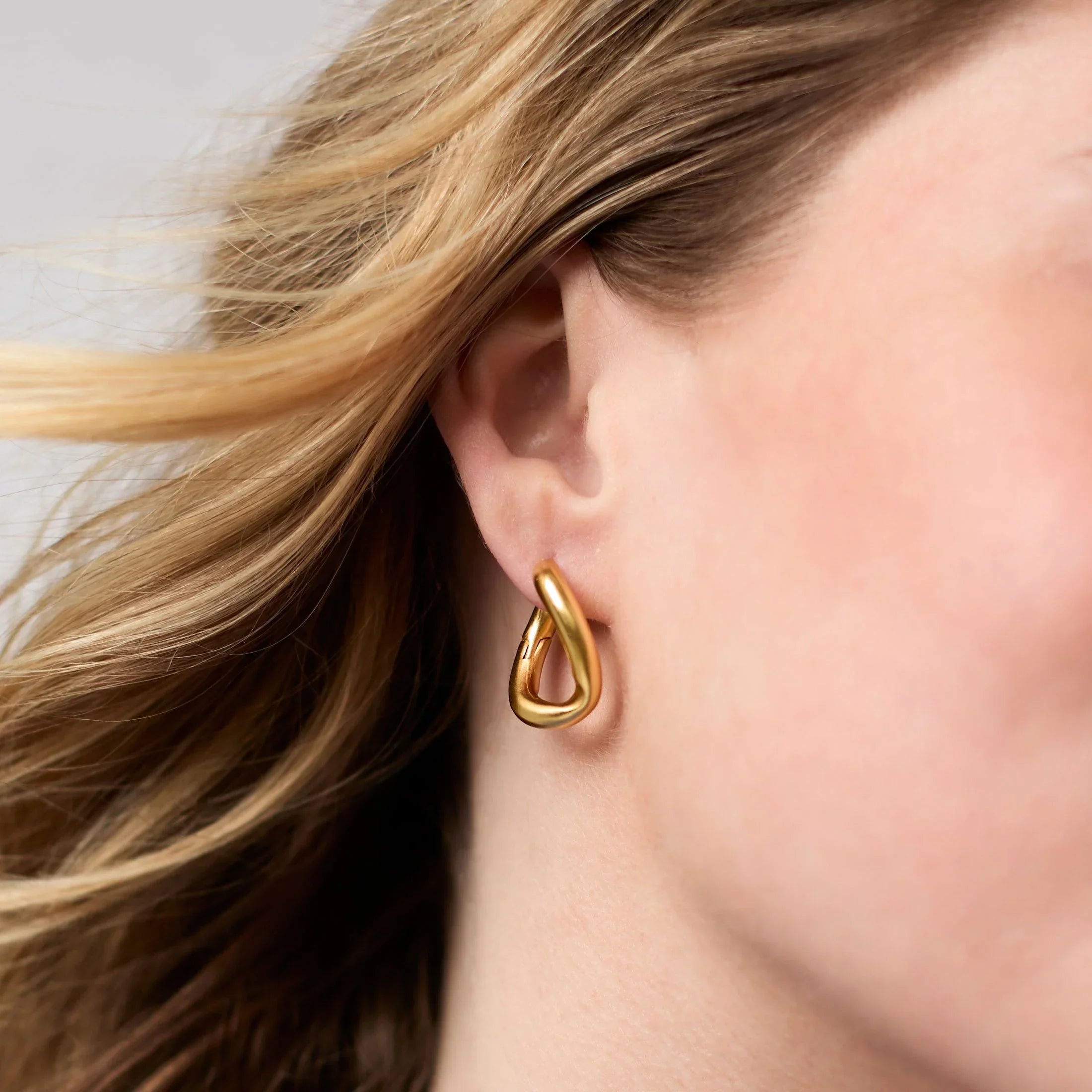 Gold earring worn by a person with blonde hair.
