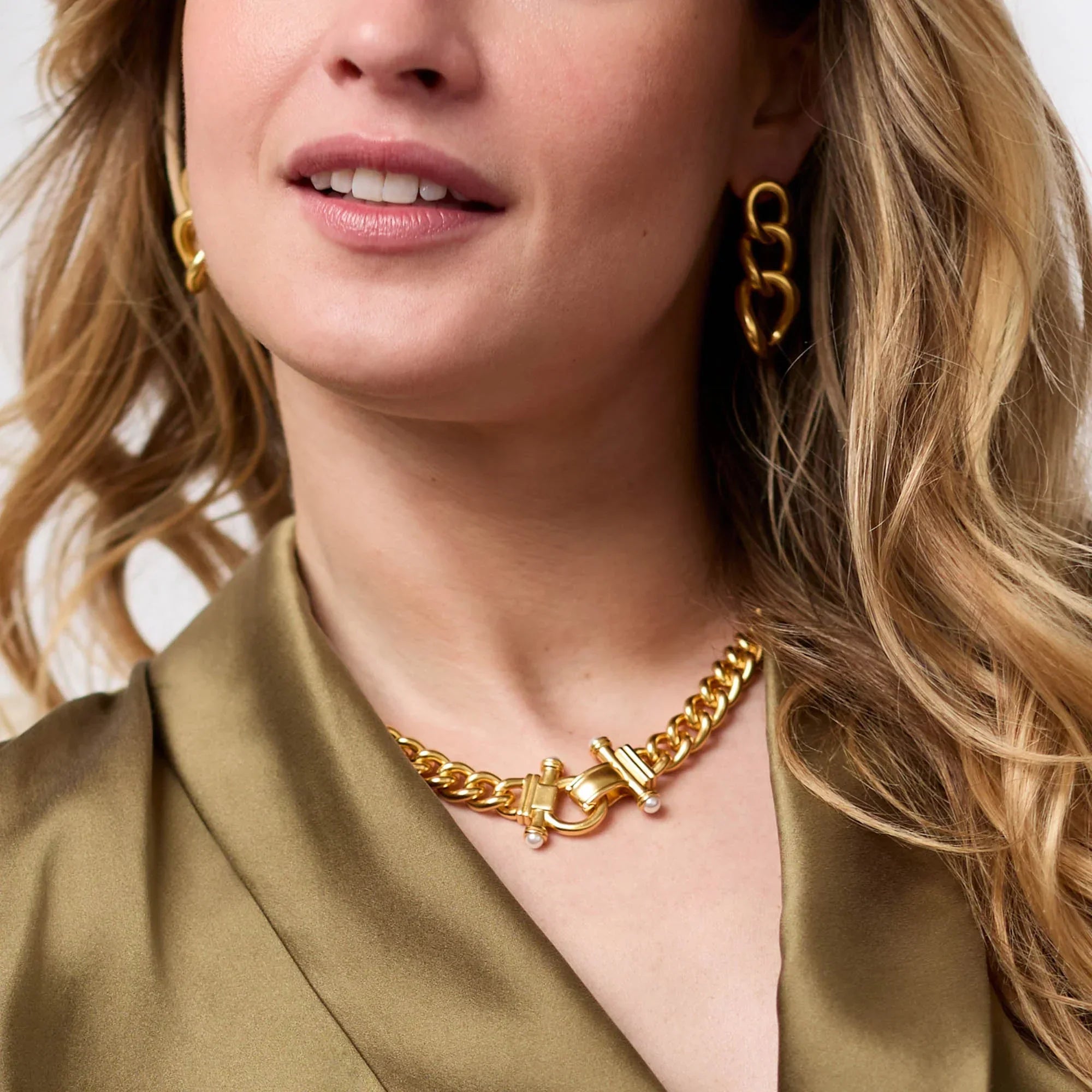 Close-up of a woman wearing a gold chain necklace and earrings against a neutral background