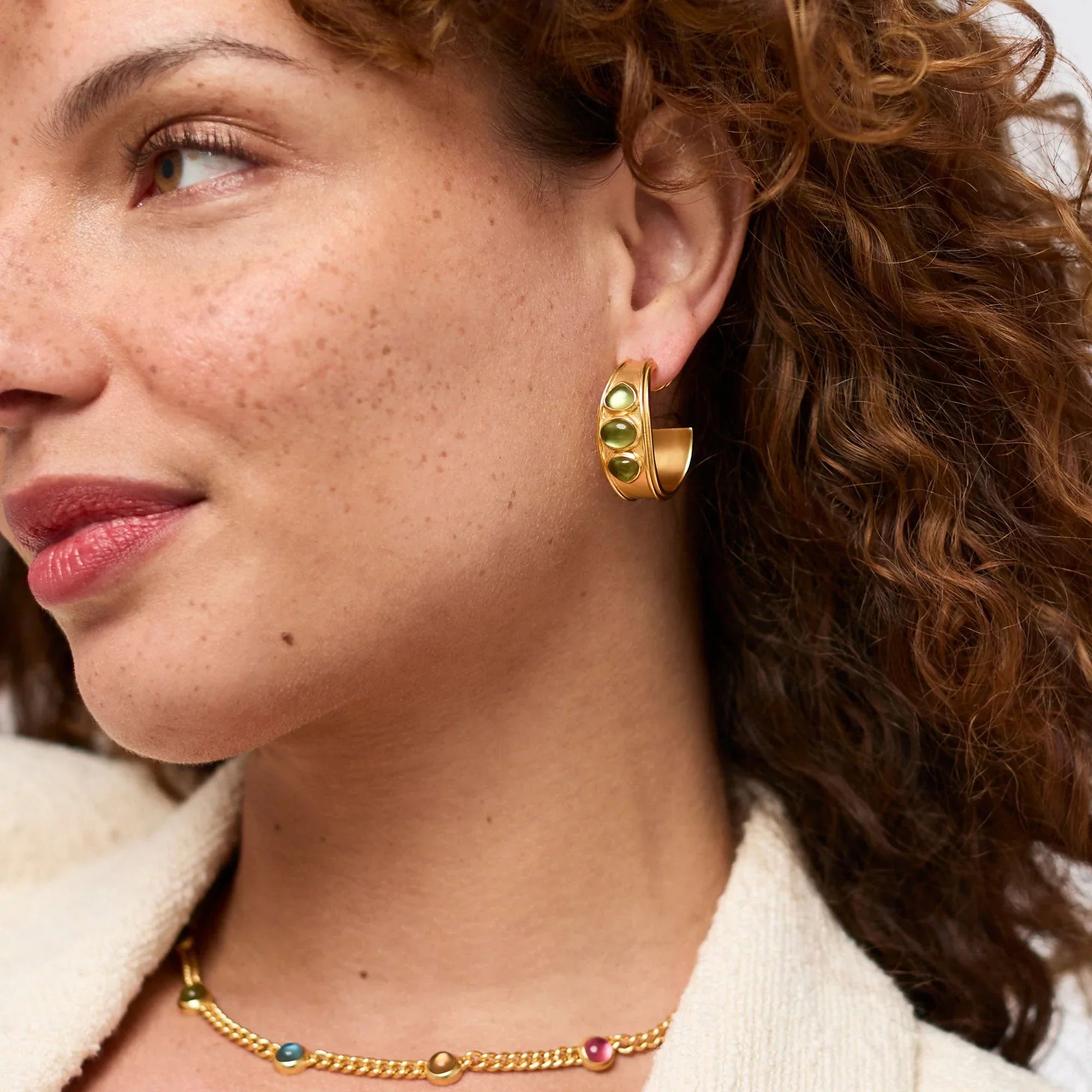 Close-up of a woman wearing gold hoop earrings and a necklace with a neutral background