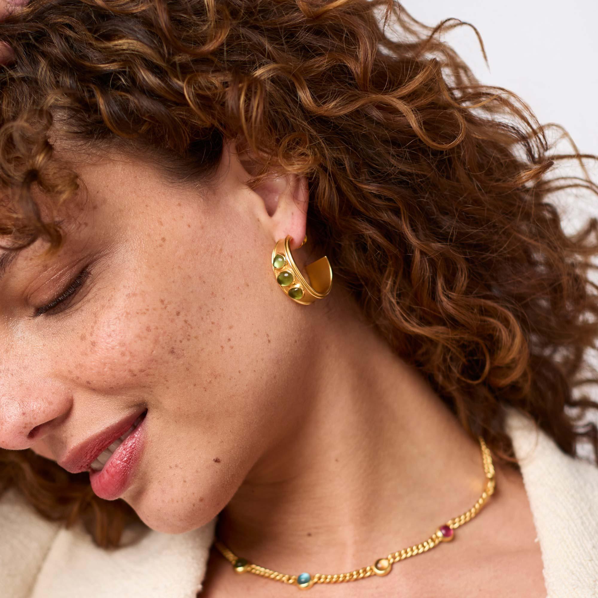 Close-up of a woman wearing gold earrings and necklace with a neutral background