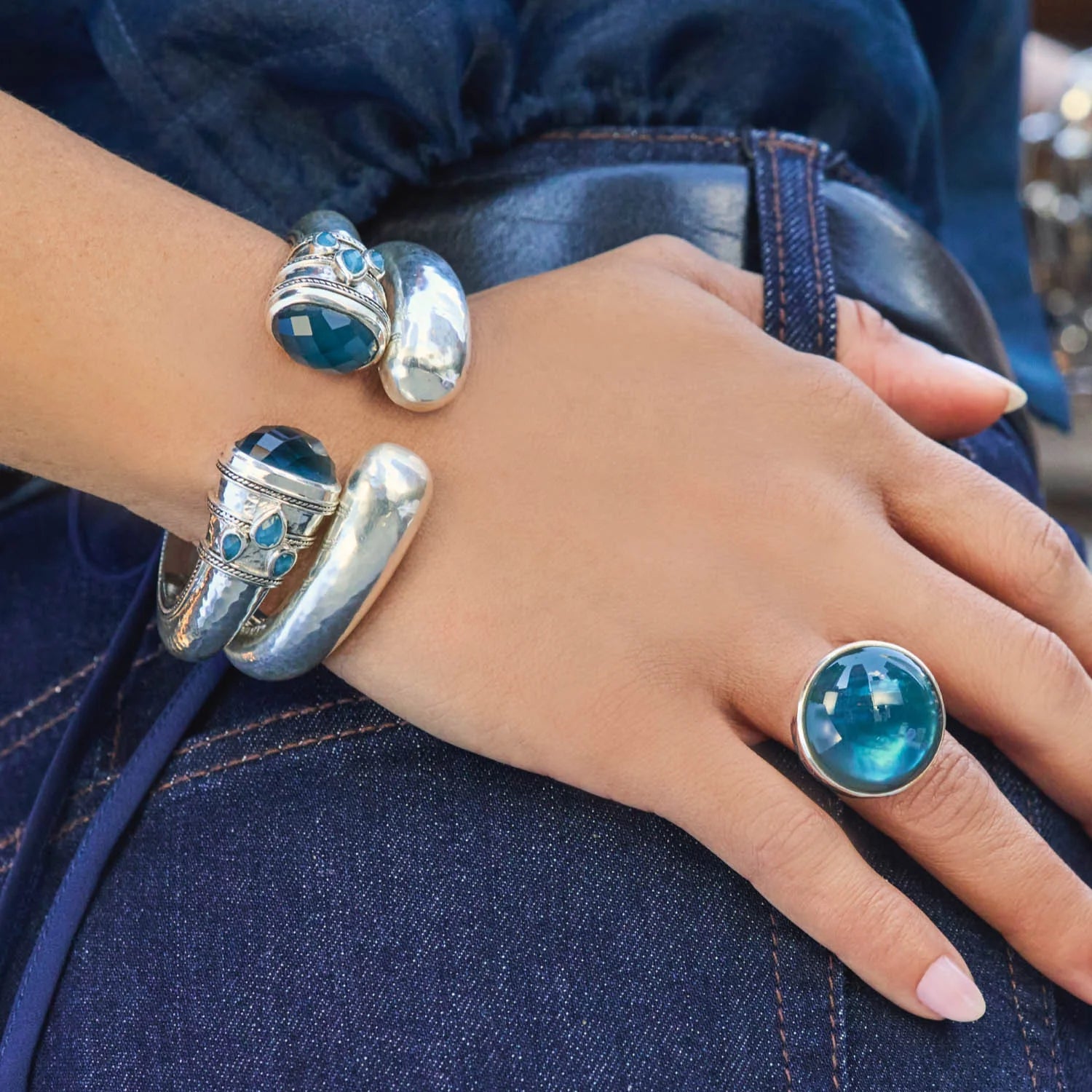 Hand wearing multiple silver rings with blue gemstones on a denim background