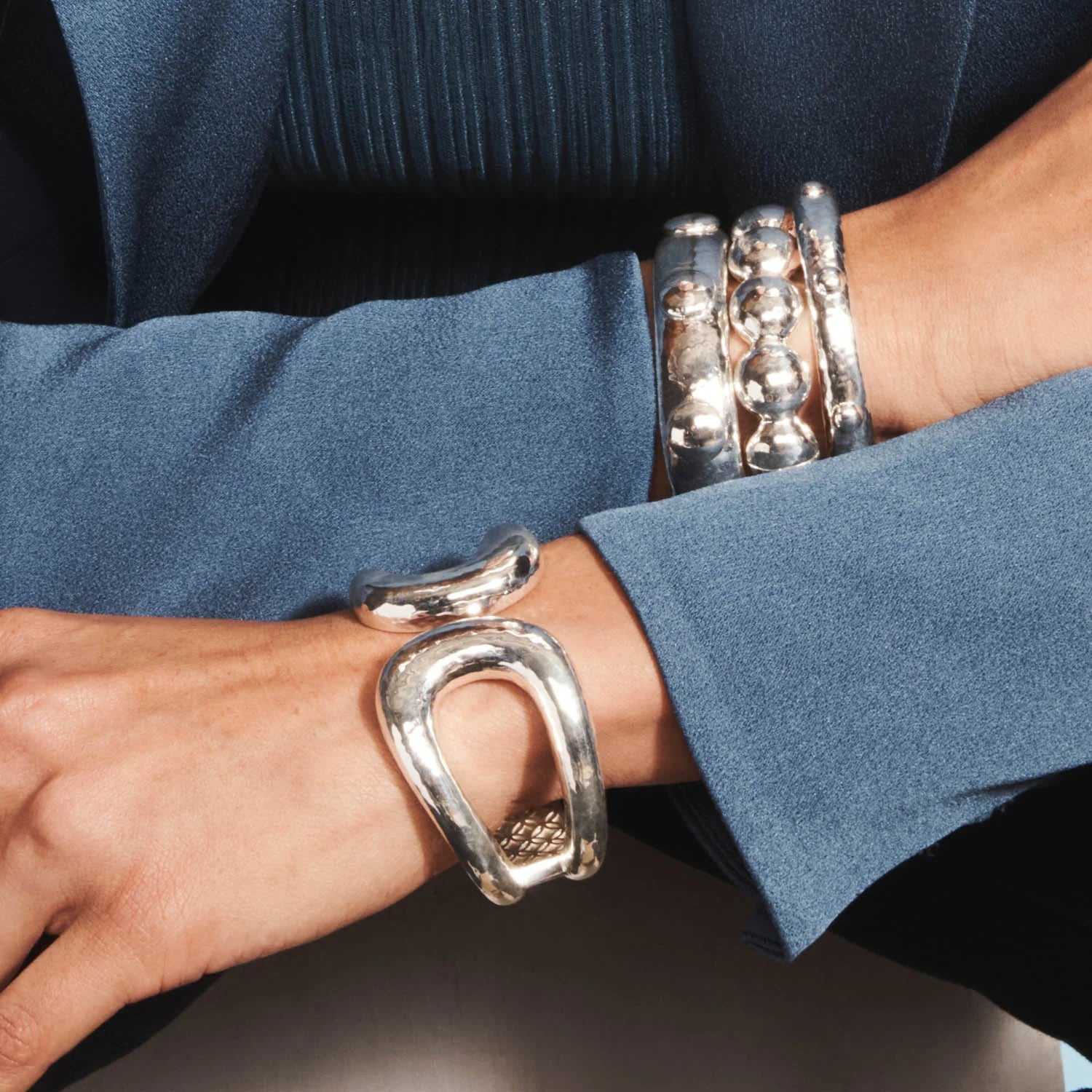 Close-up of a person's wrist wearing multiple silver bracelets on a dark background