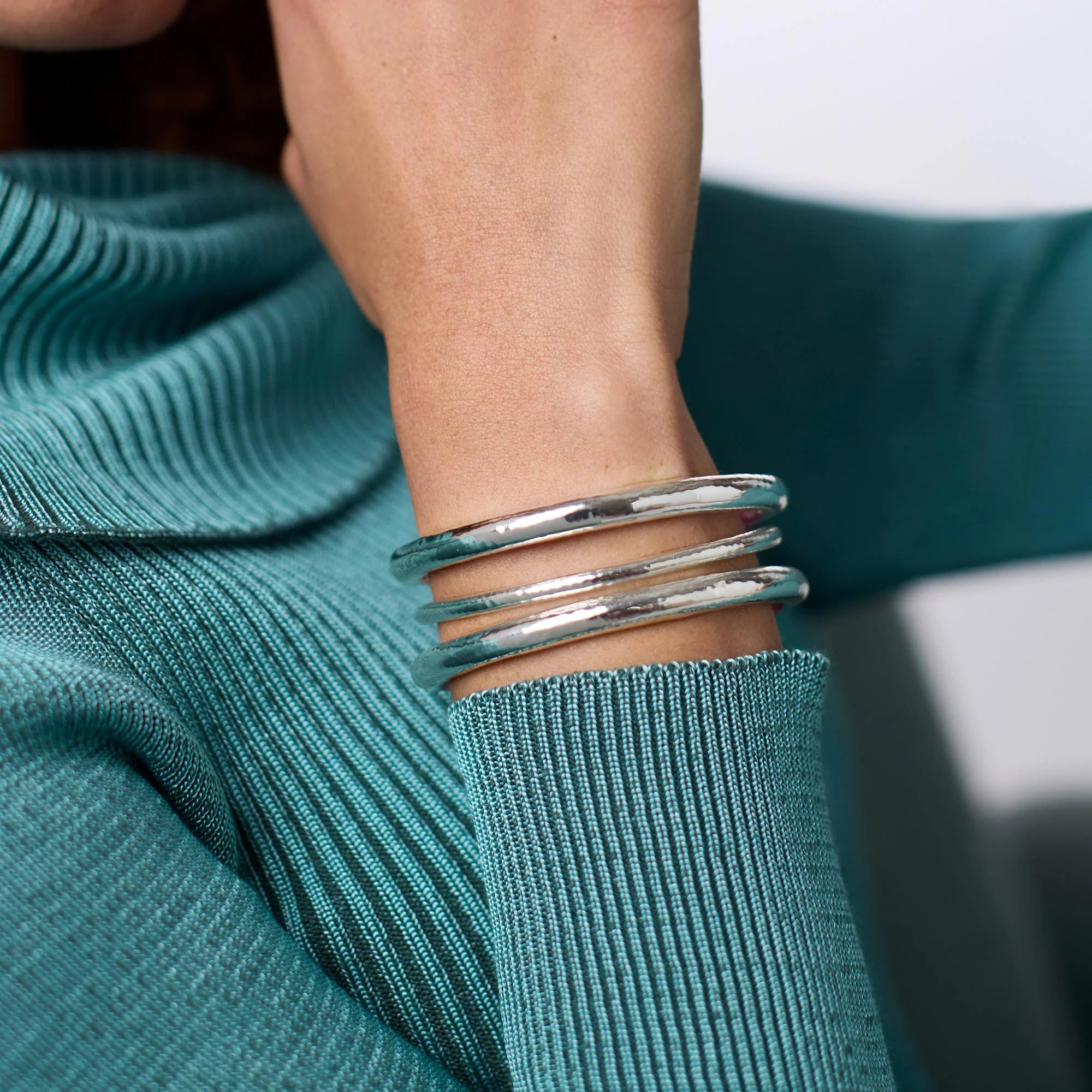 Silver bangles on a person's wrist with a teal sweater