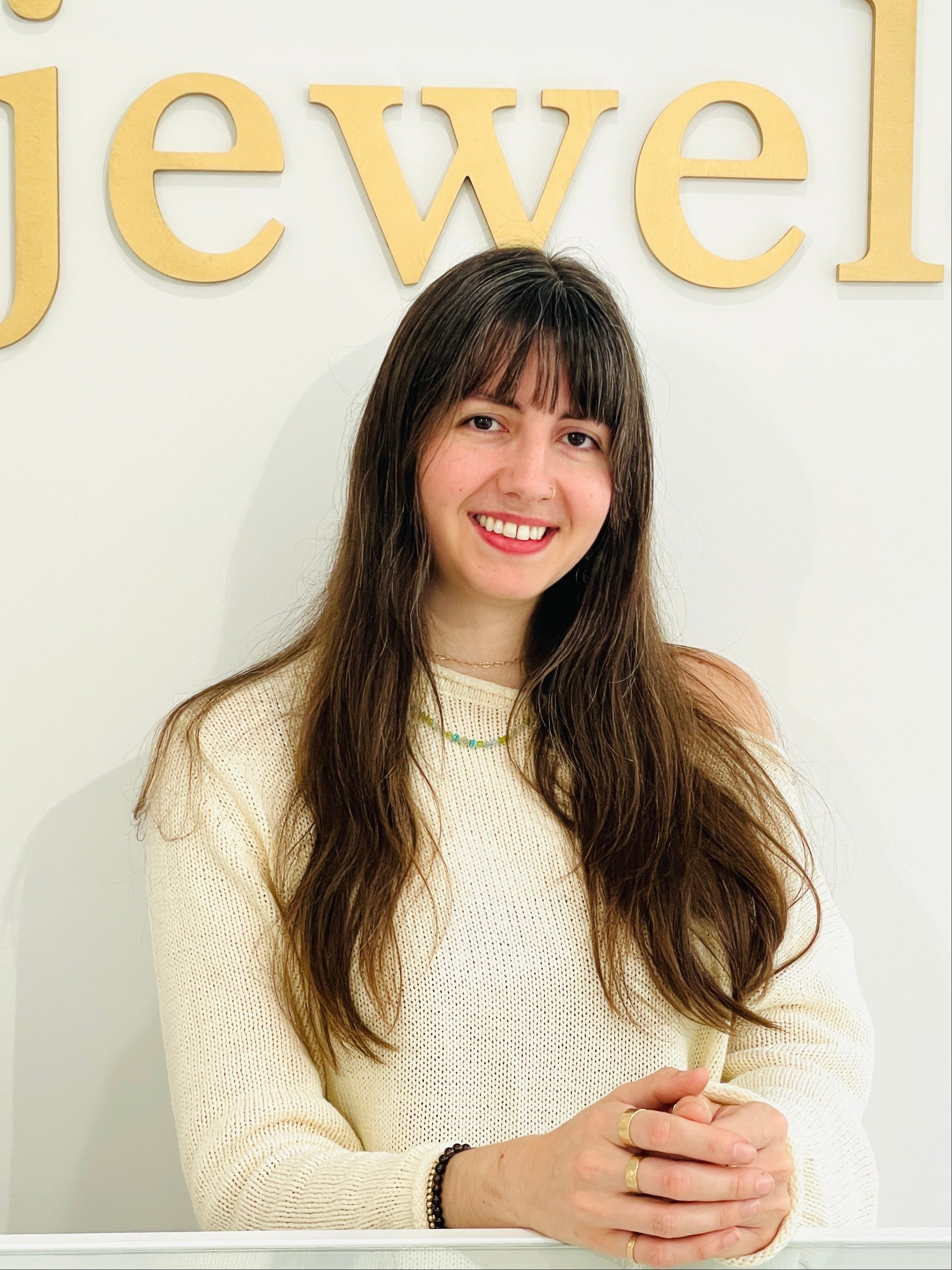 Woman in a white sweater standing in front of a 'jewel' sign.