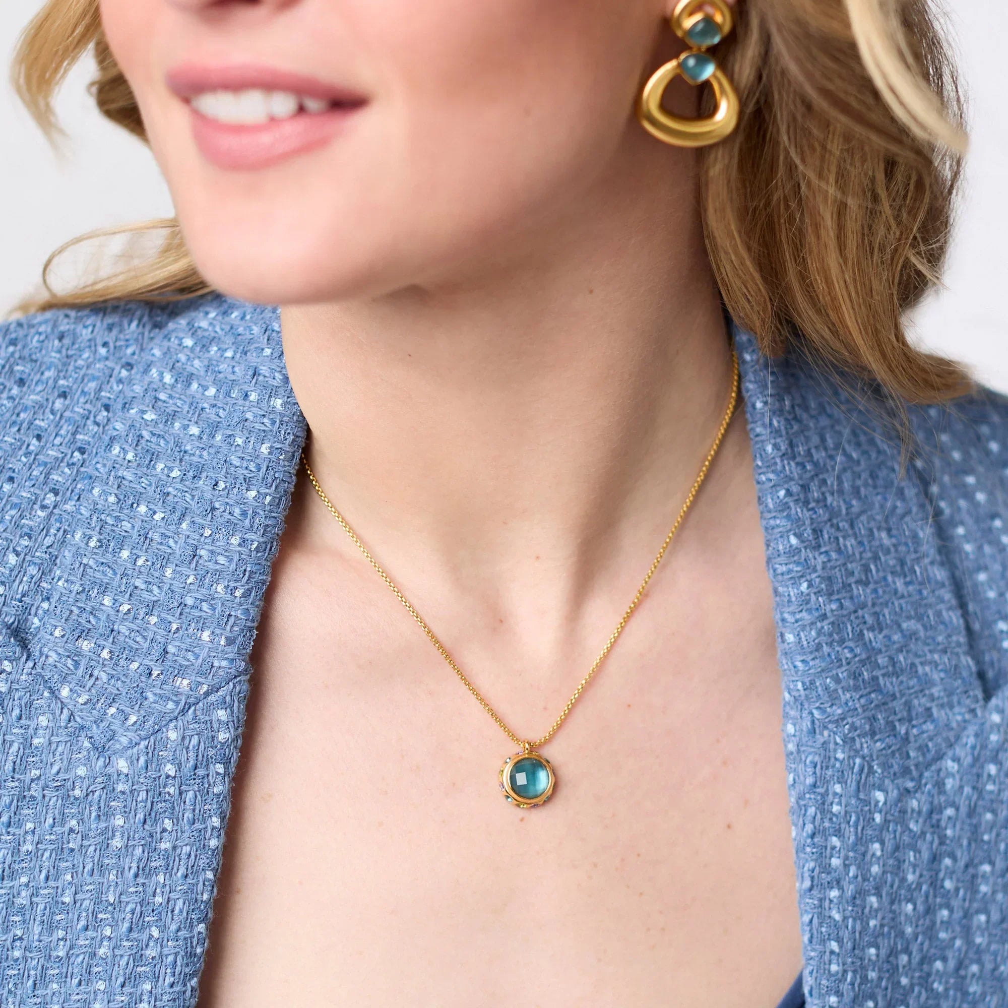 Woman wearing a gold necklace with a blue gemstone and matching earrings.