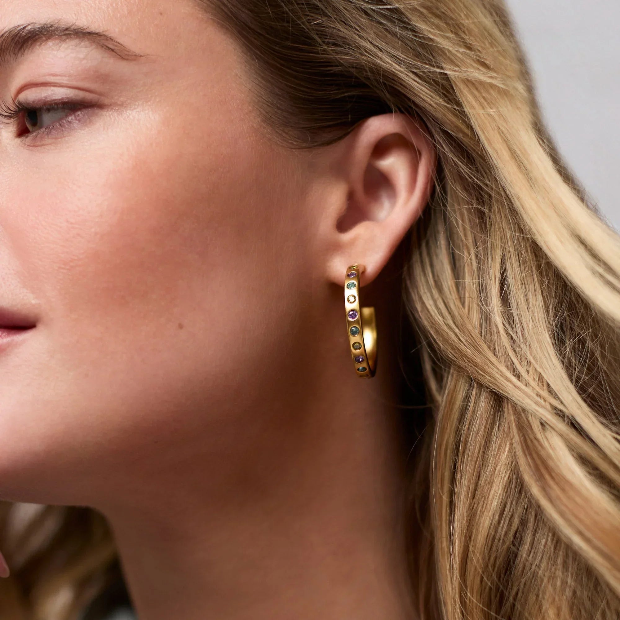 Close-up of a woman wearing gold hoop earrings with colorful stones.
