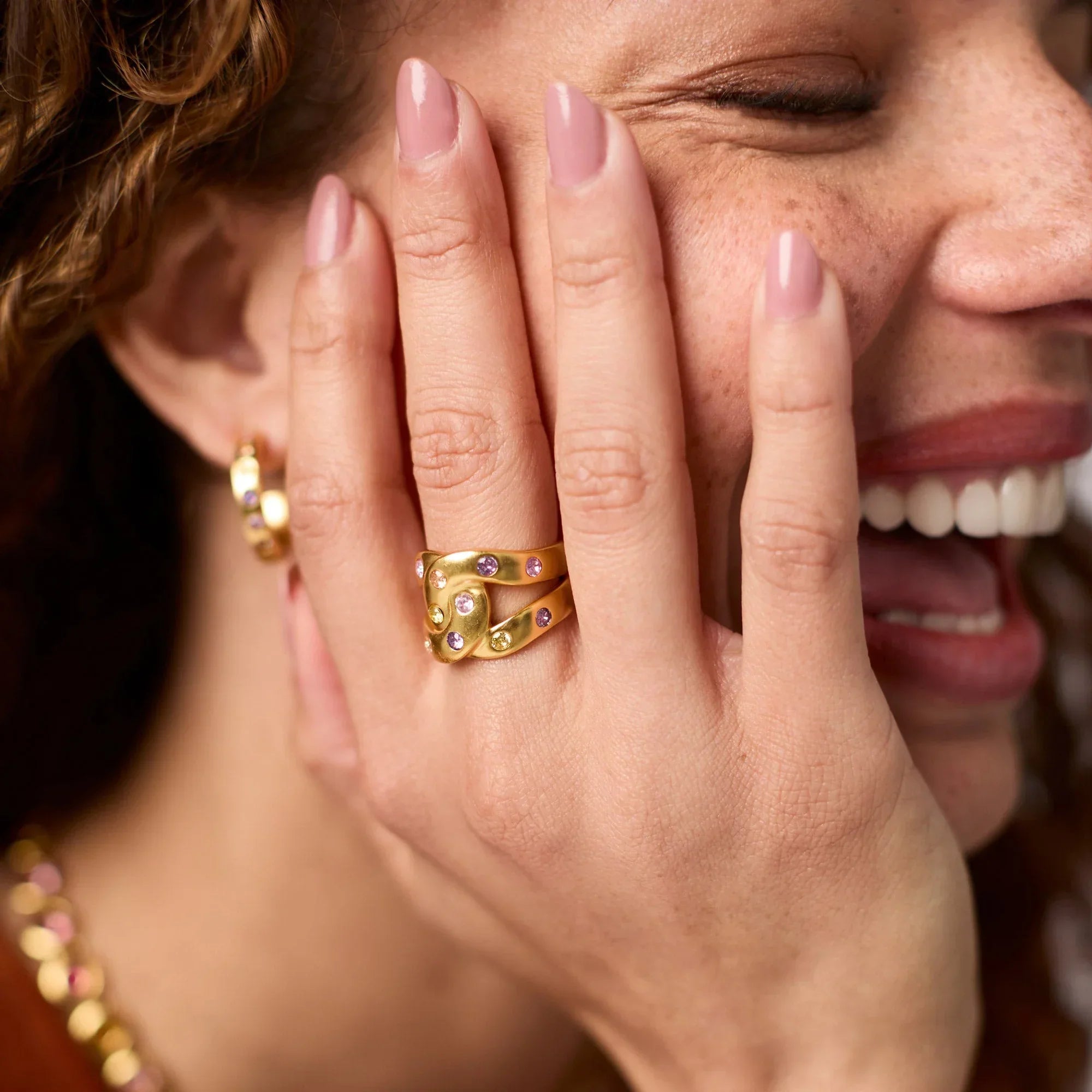 Woman wearing gold rings and earrings, covering her face with her hand.