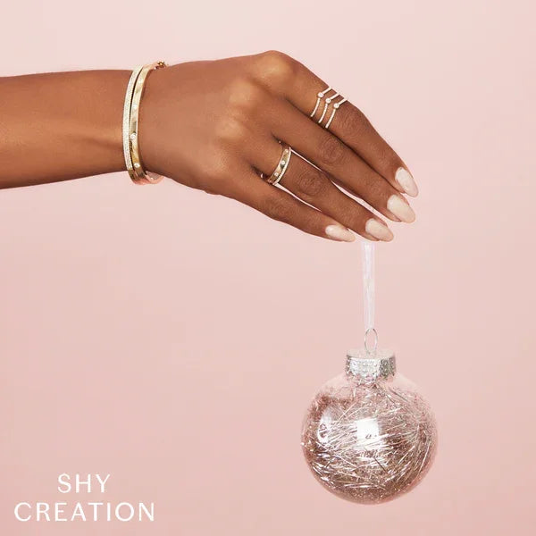 Hand holding a silver ornament against a pink background with 'SHY CREATION' branding.
