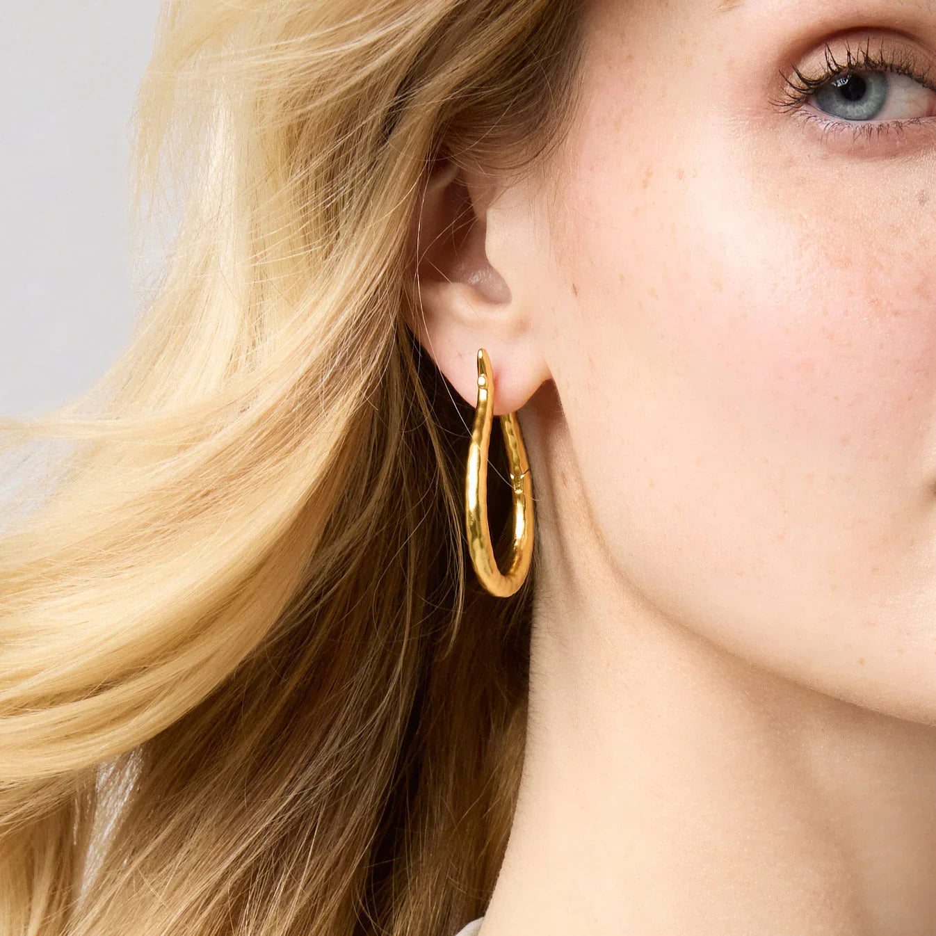 Close-up of a person wearing gold hoop earrings with blonde hair.