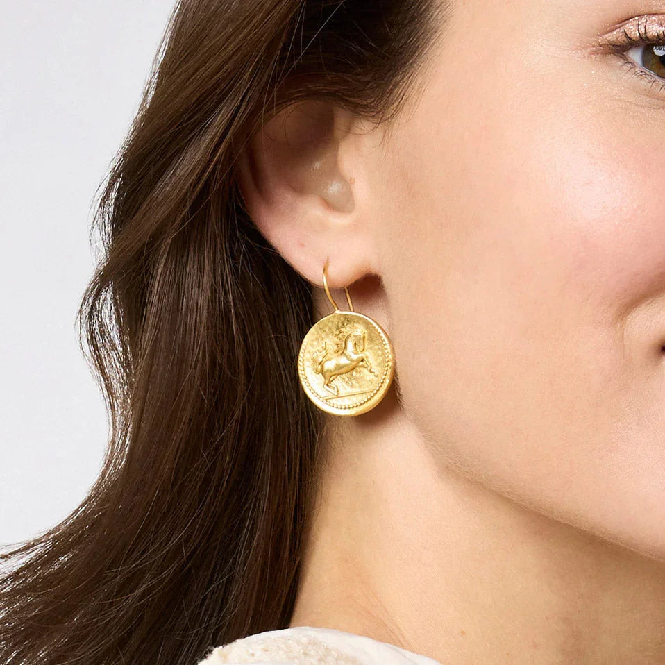 Close-up of a woman wearing gold earrings with a plain background