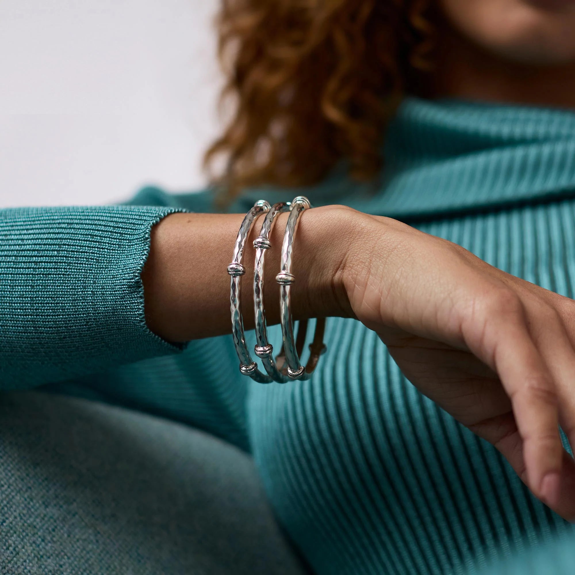 Close-up of a person wearing silver bracelets on a teal sweater.