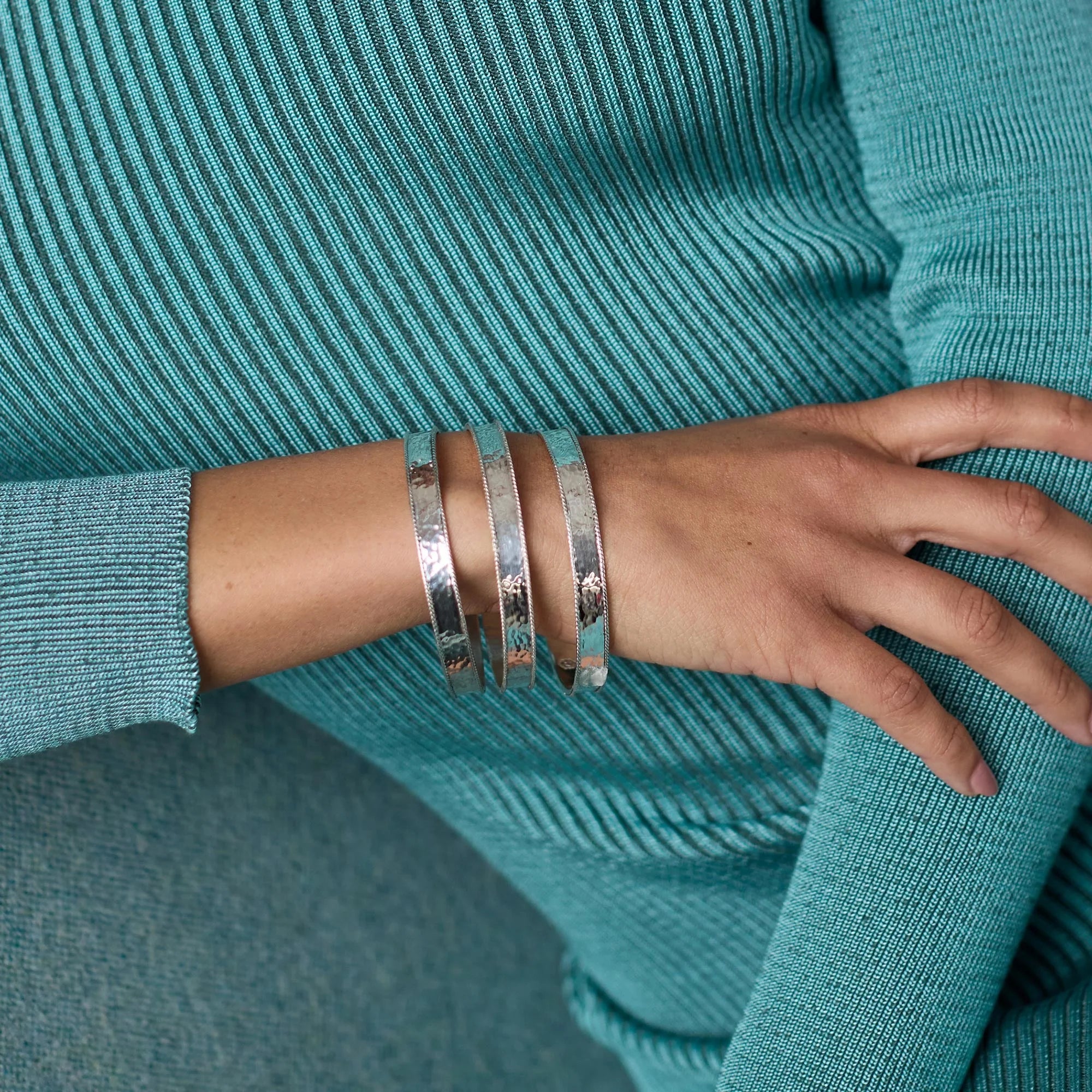 Close-up of a person wearing silver bracelets on a teal sweater.