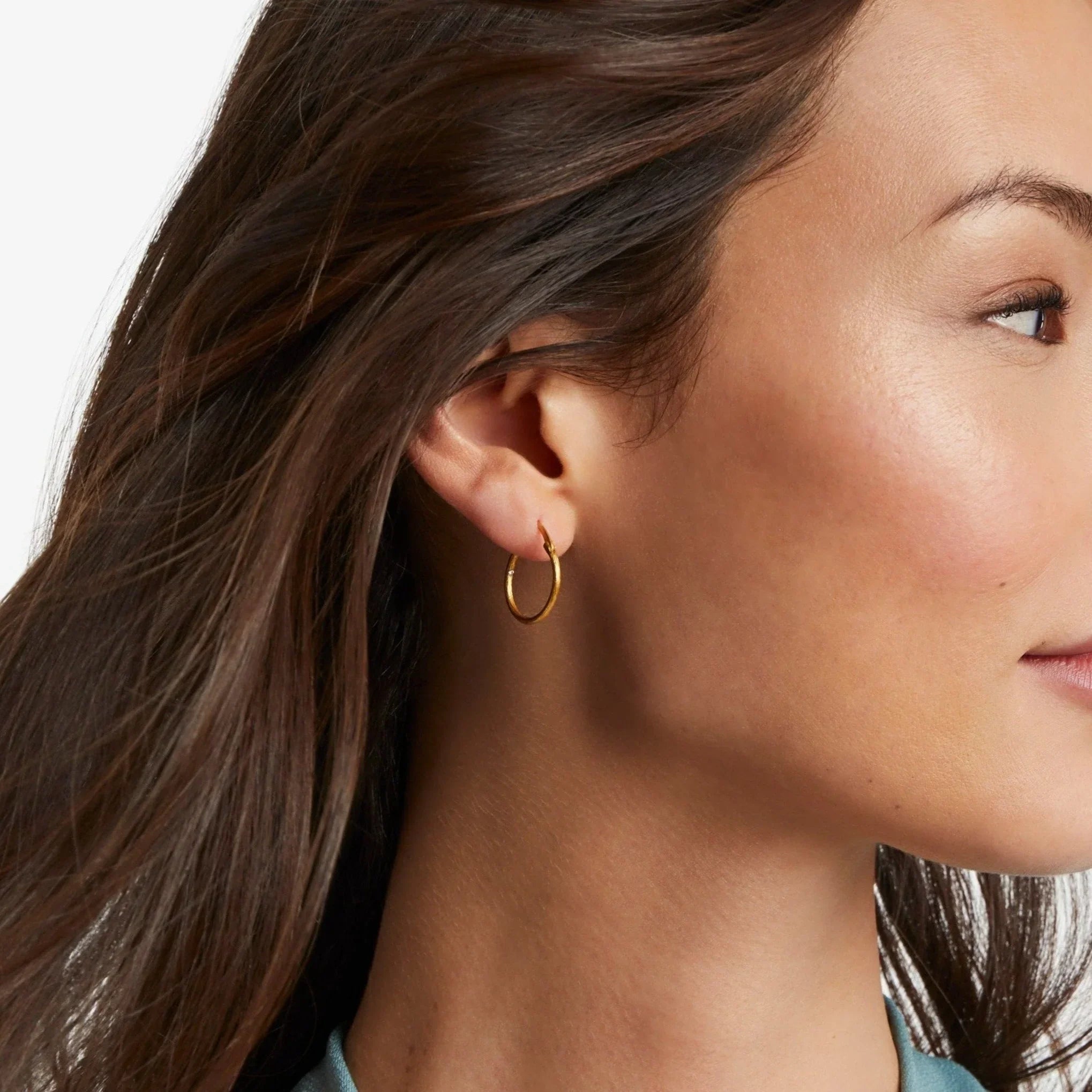 Close-up of a woman wearing a gold hoop earring with a neutral background