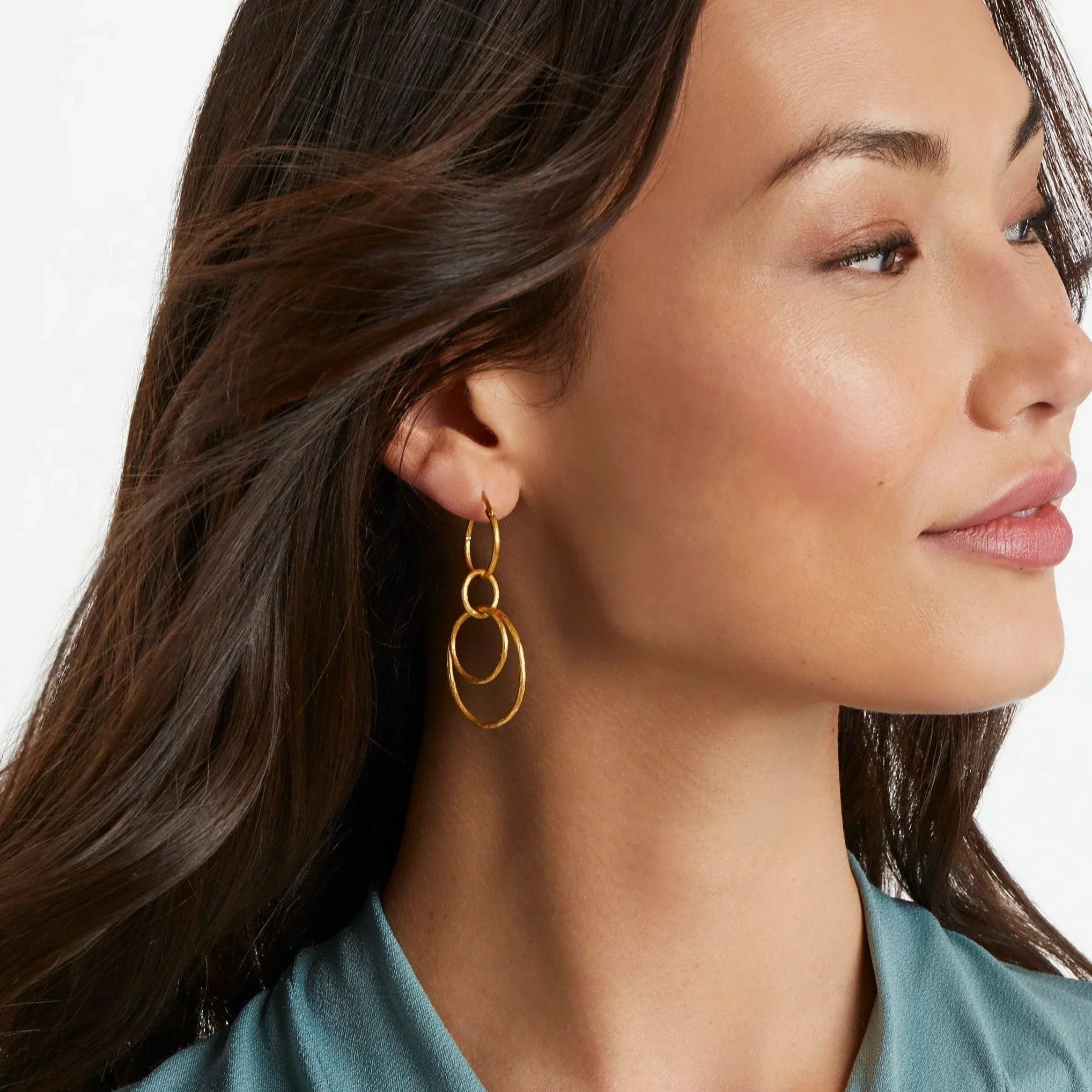 Close-up of a woman wearing gold hoop earrings with a plain background