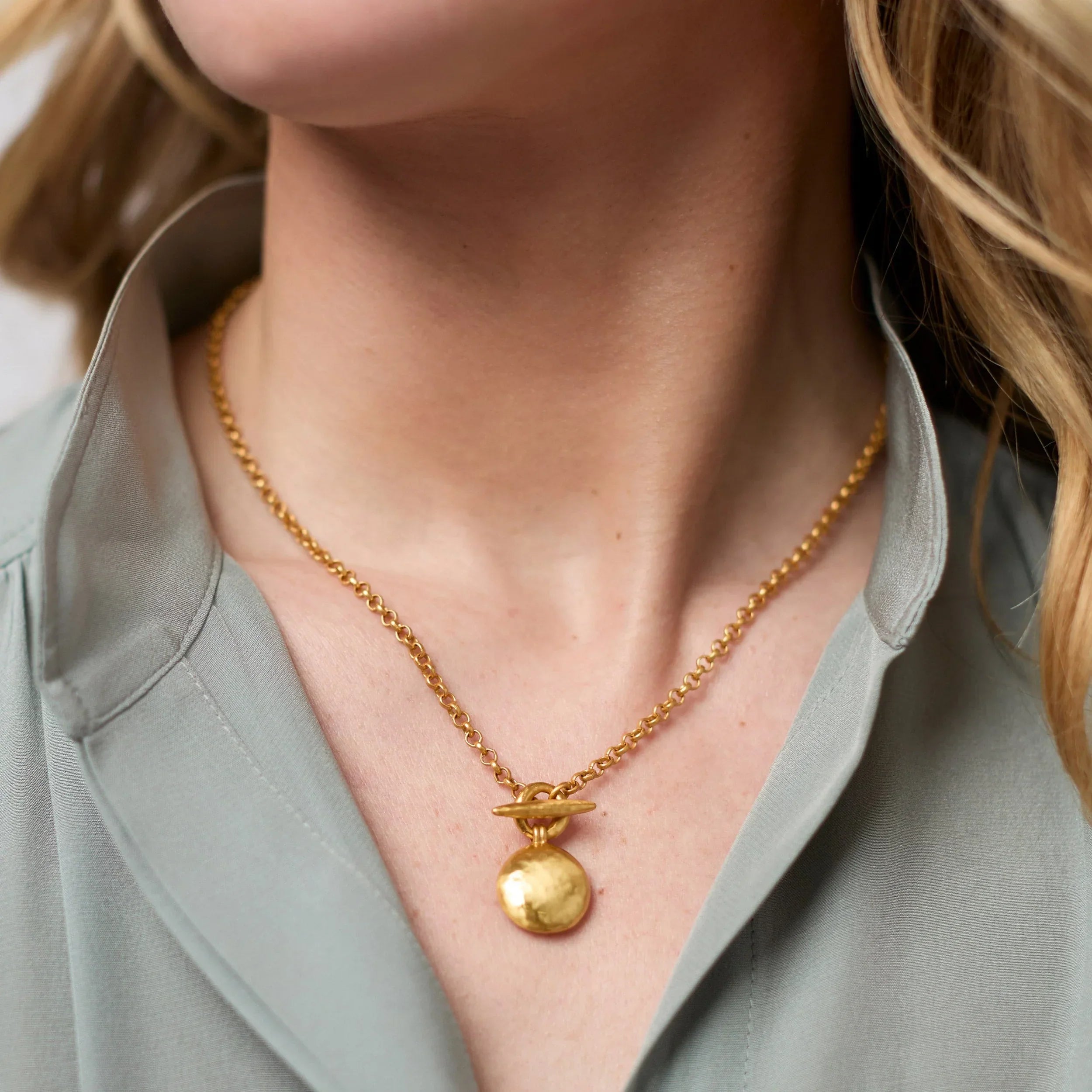 Close-up of a person wearing a gold necklace with a pendant.