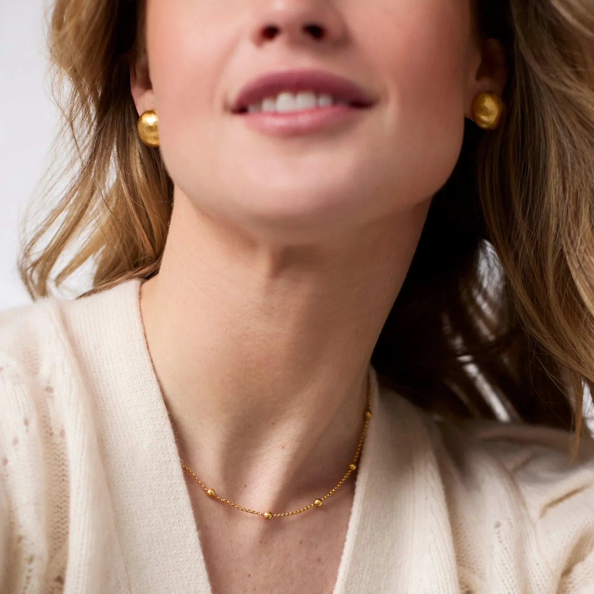 Close-up of a woman wearing gold earrings and a necklace against a neutral background