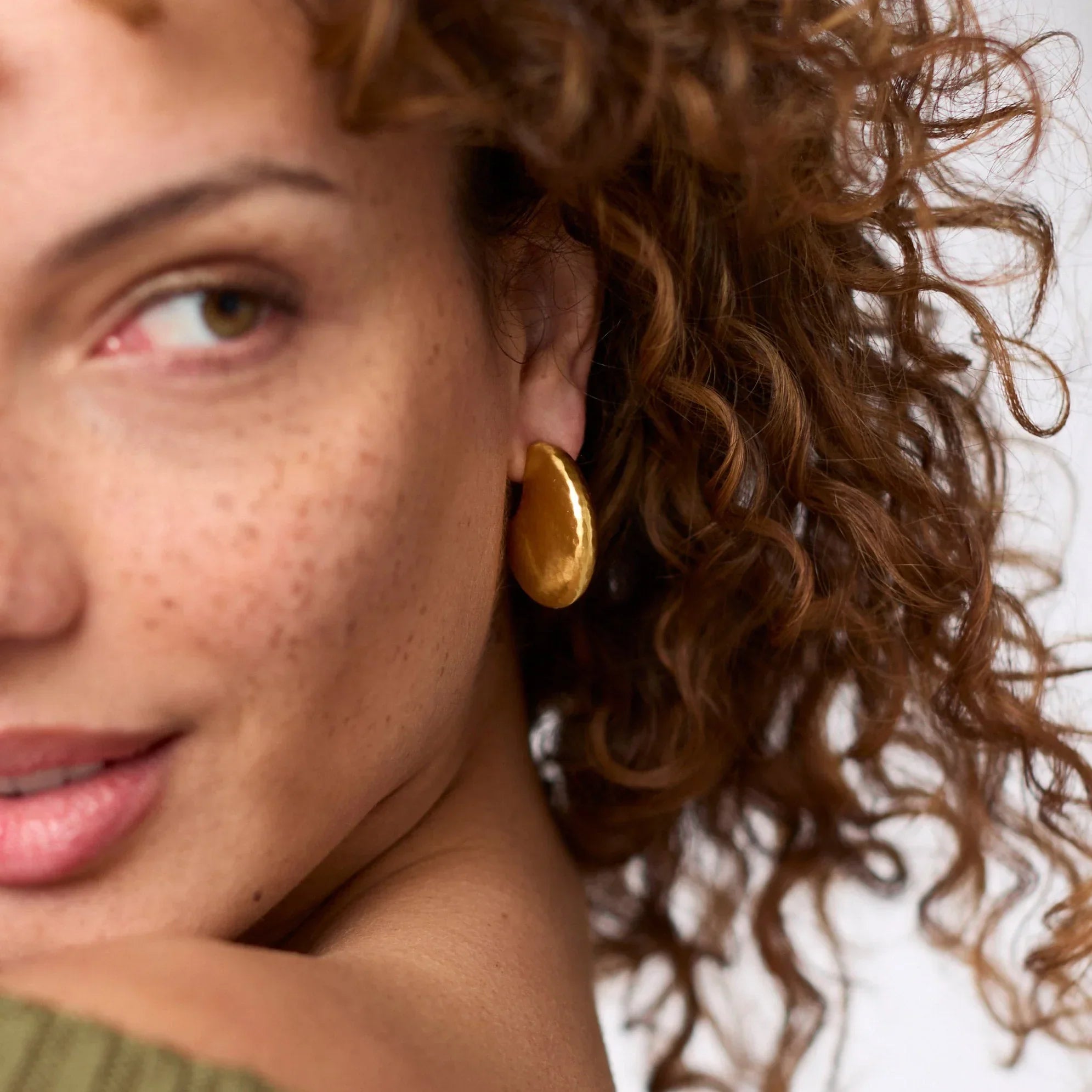 Close-up of a woman wearing gold hoop earrings with a neutral background