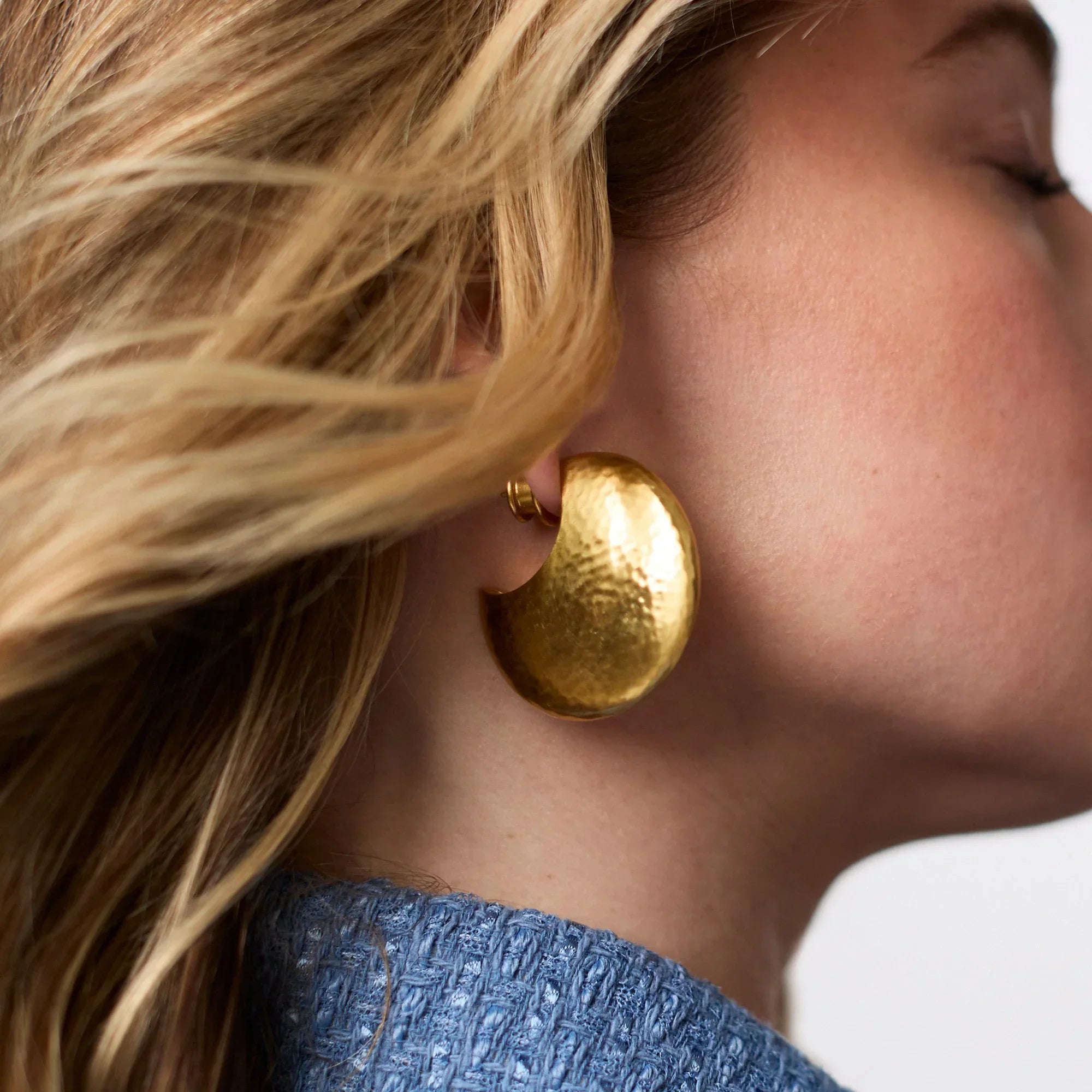 Close-up of a person wearing a gold earring with a blurred background
