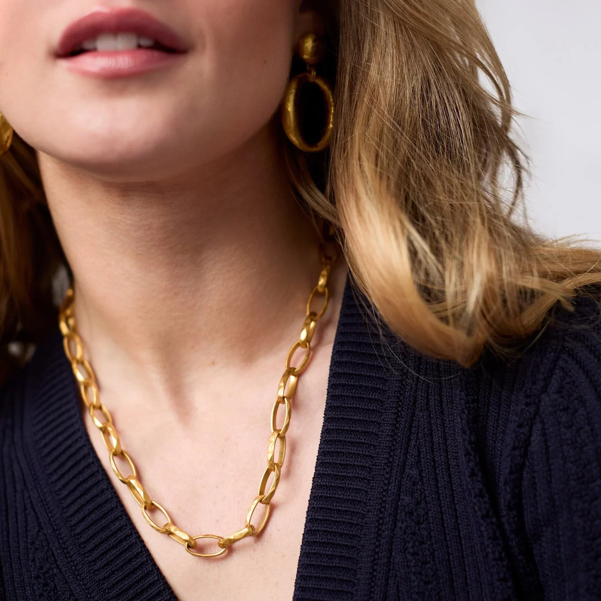 Close-up of a person wearing a gold chain necklace and earrings.