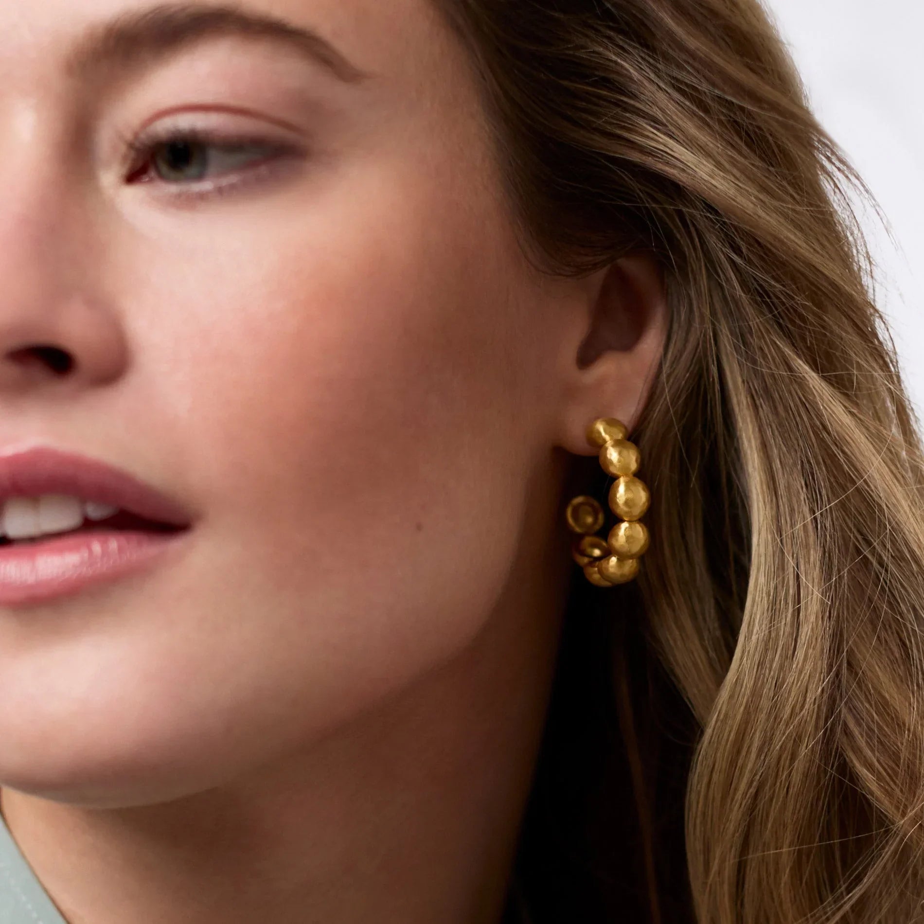 Close-up of a woman wearing gold earrings with a neutral background