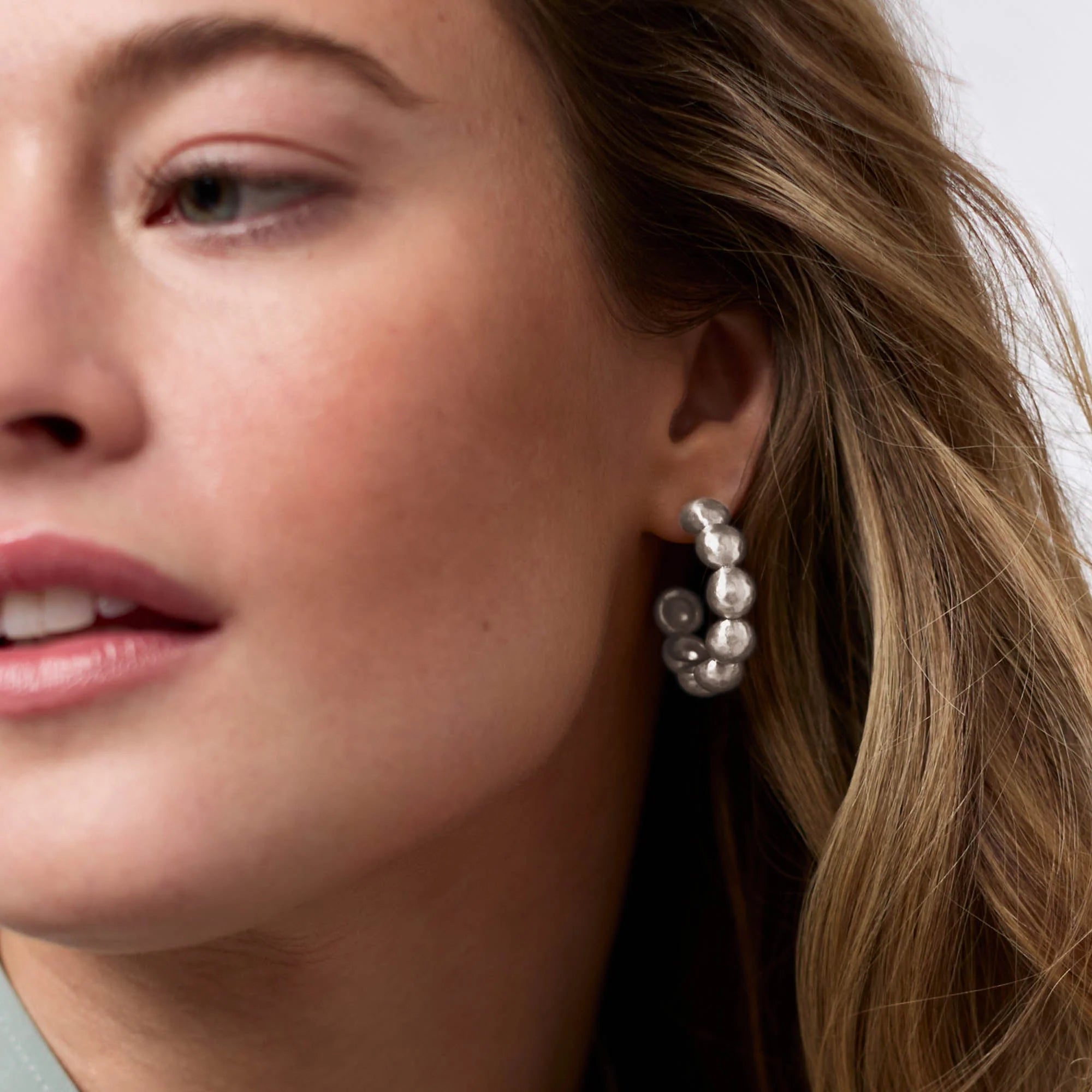 Close-up of a woman wearing silver earrings with a neutral background