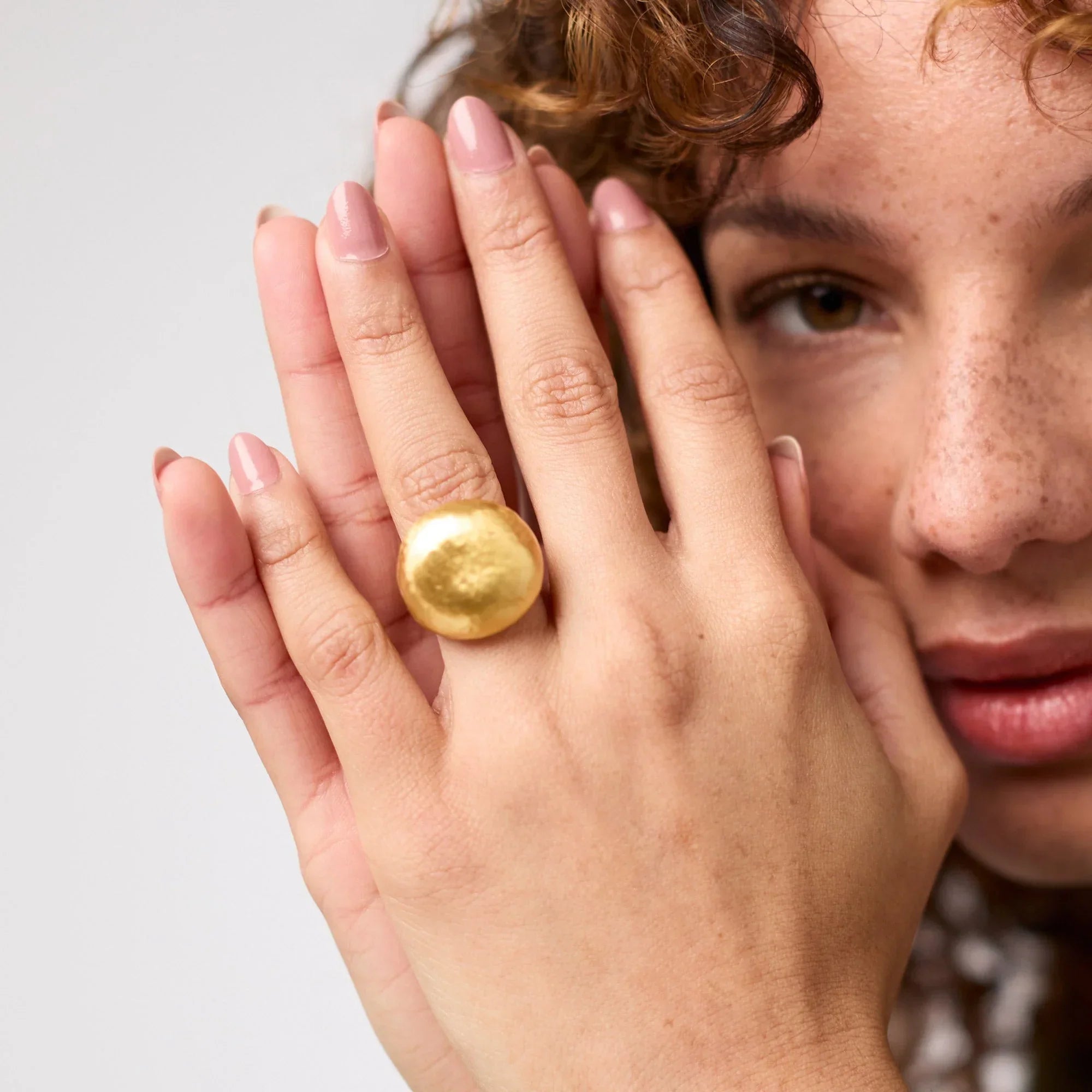 Woman wearing a gold ring on her finger against a neutral background