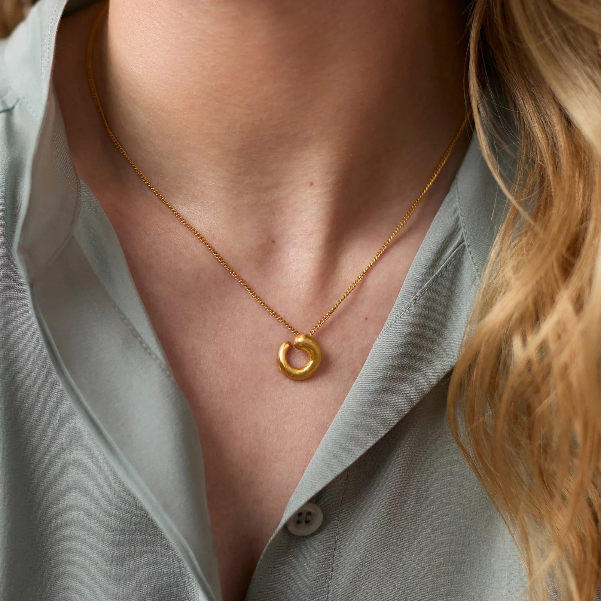 Close-up of a person wearing a gold necklace with a circular pendant.