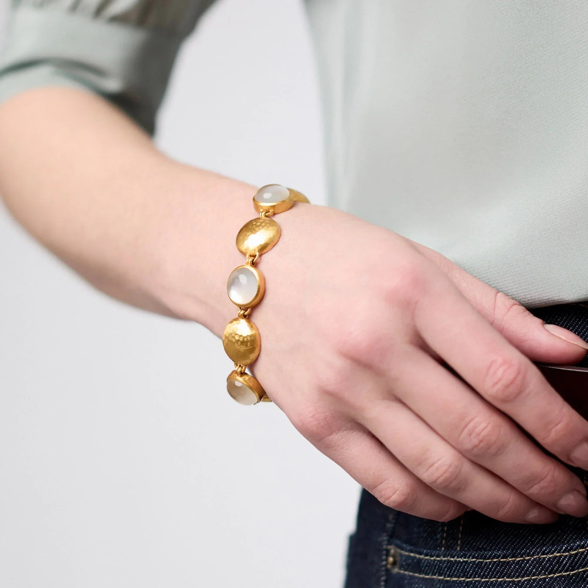Gold bracelet with large beads on a wrist against a neutral background