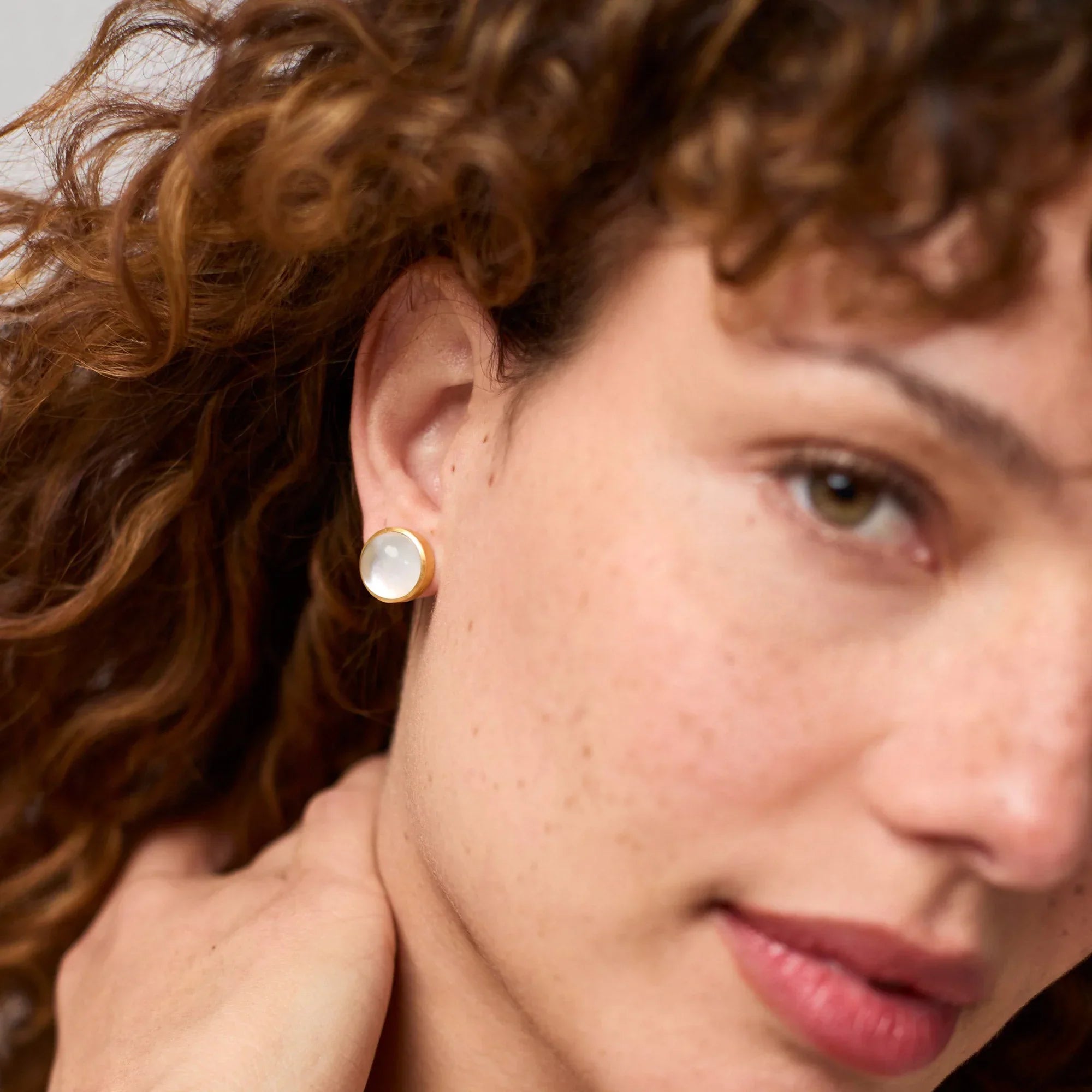 Close-up of a woman wearing a round earring with a neutral background