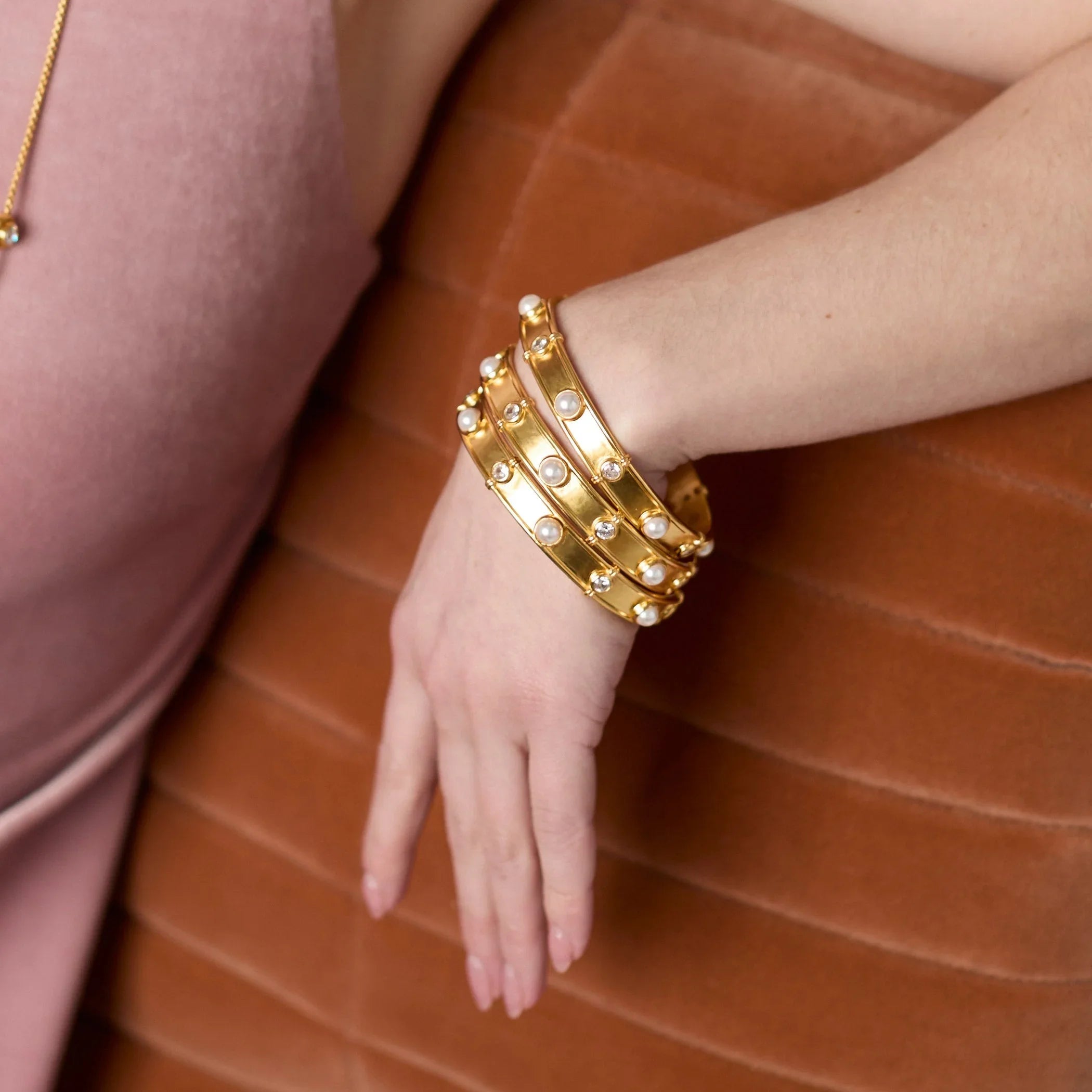 Gold bangles on a hand against a brown background