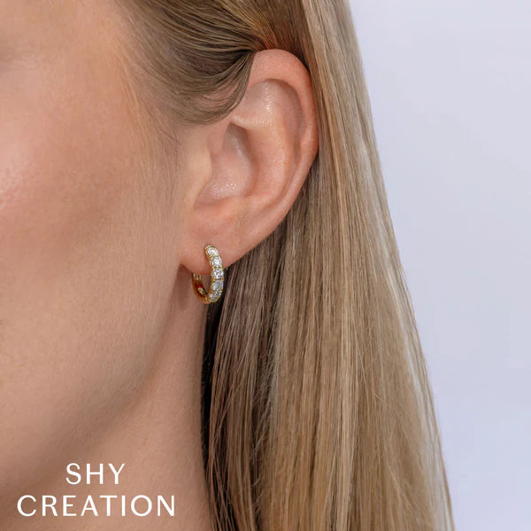 Close-up of an ear wearing a gold hoop earring with 'SHY CREATION' branding.
