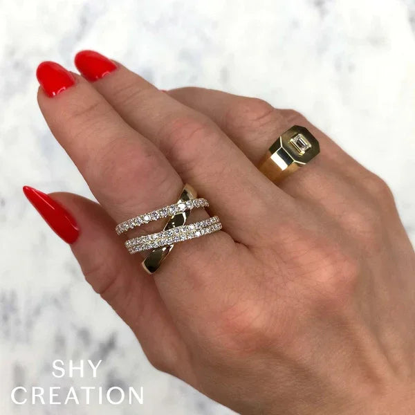 Hand wearing multiple rings with red nail polish on a light background, featuring the brand 'SHY CREATION'.