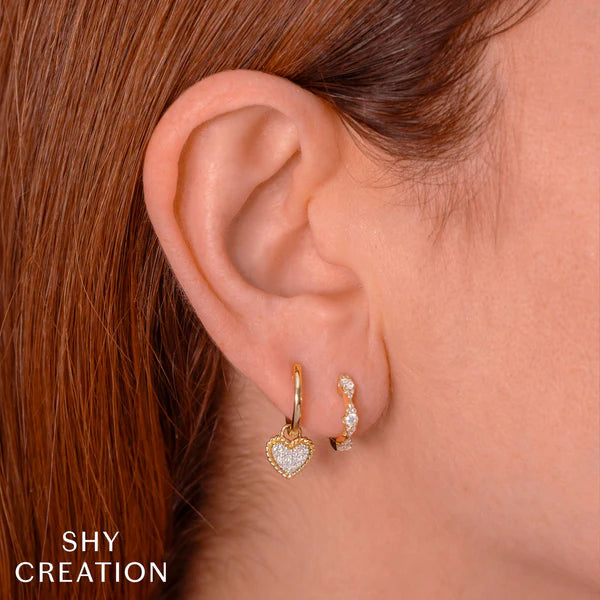 Heart-shaped earrings worn by a person with red hair, branded 'SHY CREATION'.