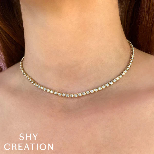 Gold necklace with clear stones on a person's neck, branded 'SHY CREATION'.