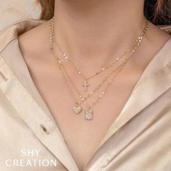 Necklace with various pendants on a person wearing a beige shirt, branded 'SHY CREATION'.