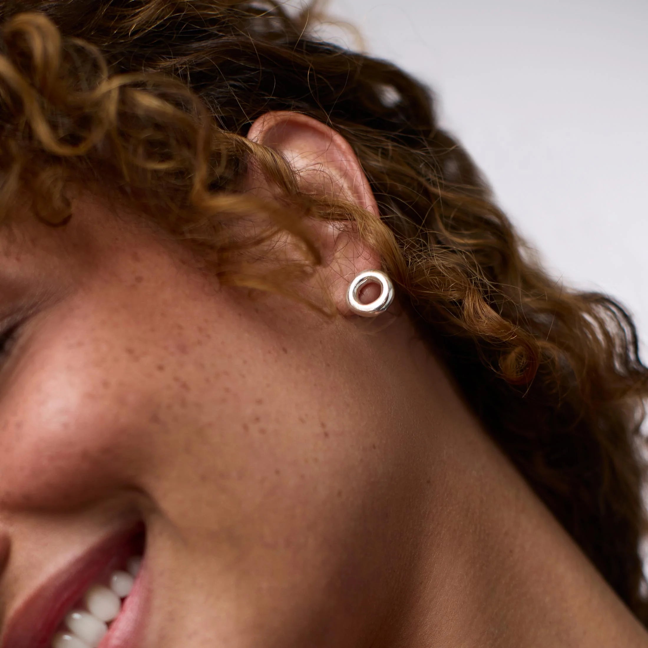 Close-up of a person wearing a silver hoop earring with a blurred background